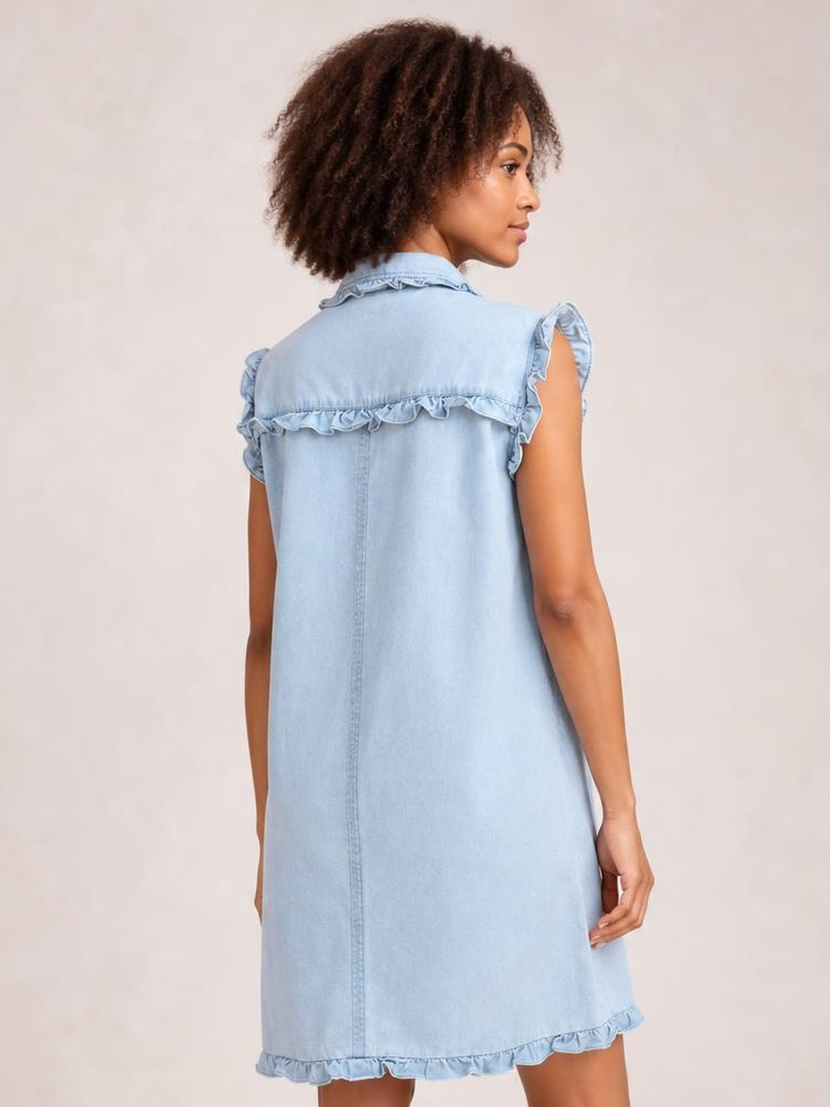 Model shown from behind in a light blue denim shift dress with a collared neckline, ruffled cap sleeves, back yoke, center seam, and ruffled hem.