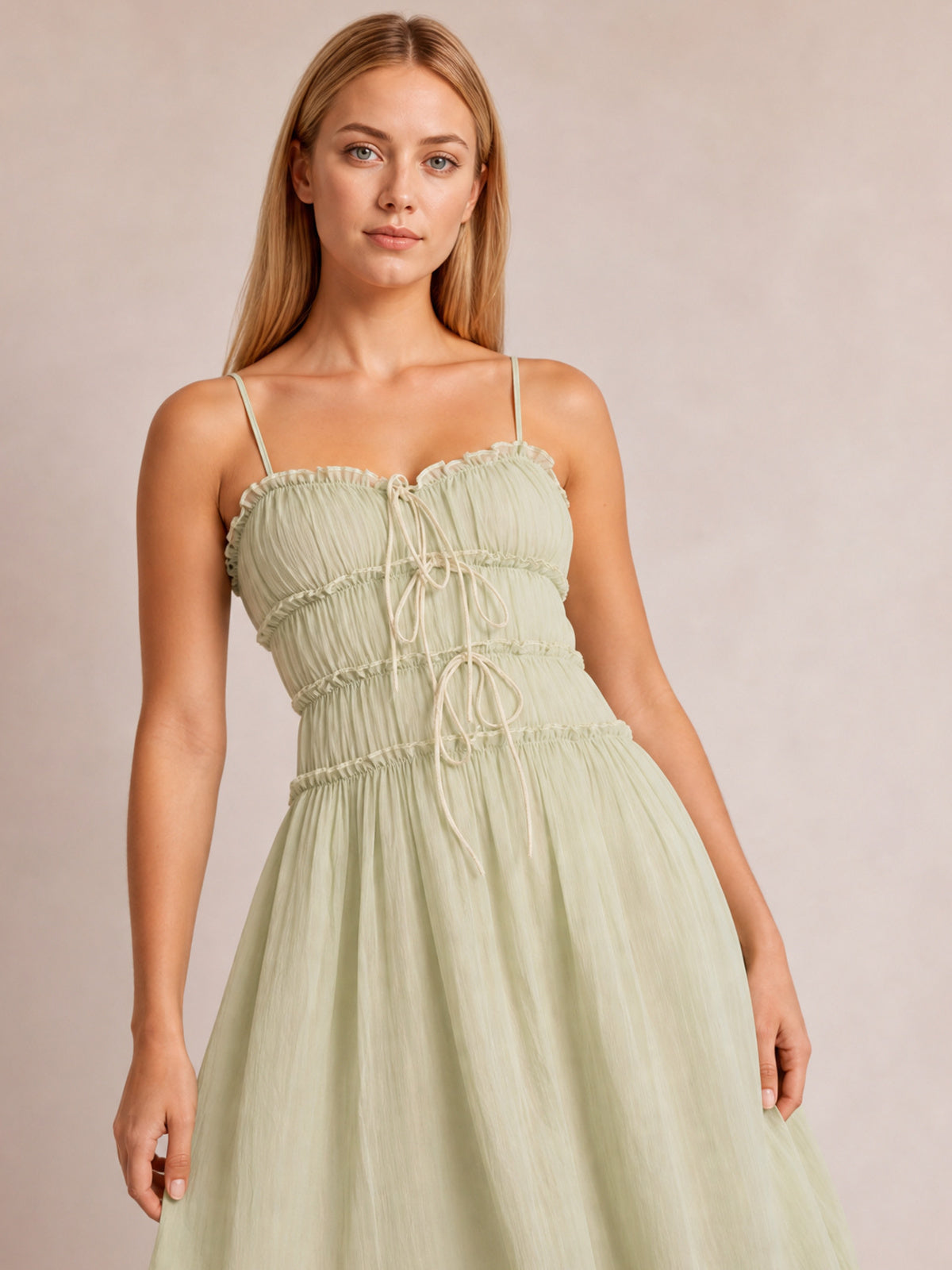 Model in a light green frill midi cami dress with spaghetti straps, a softly gathered bodice, front tie details, and a flowing flared silhouette.