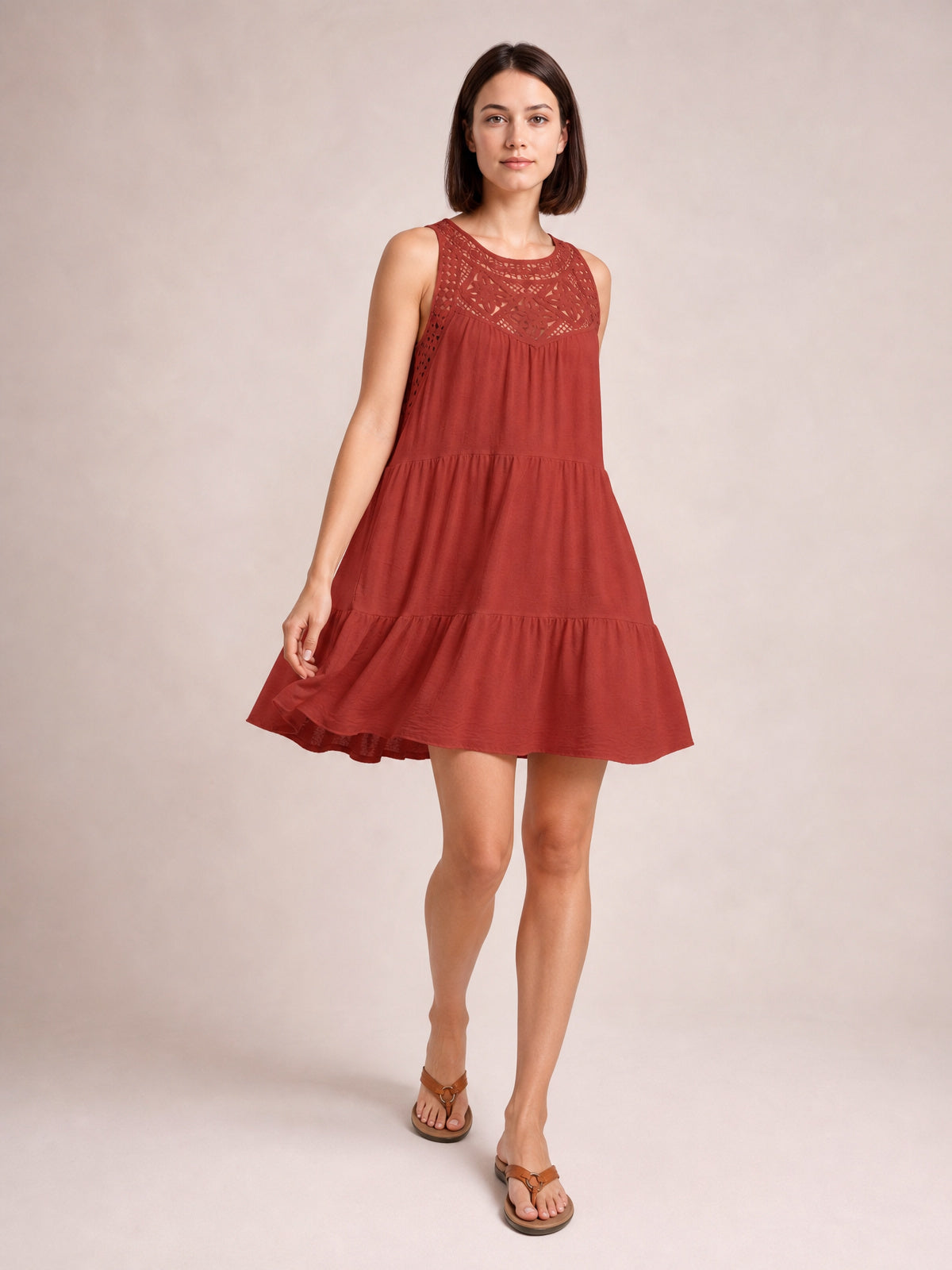 Model poses in a rust-red lace sleeveless dress with a relaxed tiered silhouette, gathered seams, flared skirt, and ruffled hem.