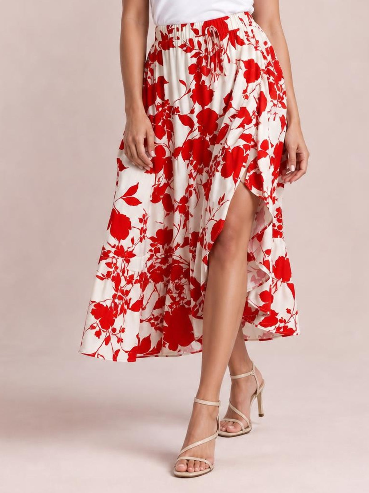 Model wears a flowy white midi skirt with a bold red floral print, elastic drawstring waist, and ruffled hem, posed with one leg stepping forward.