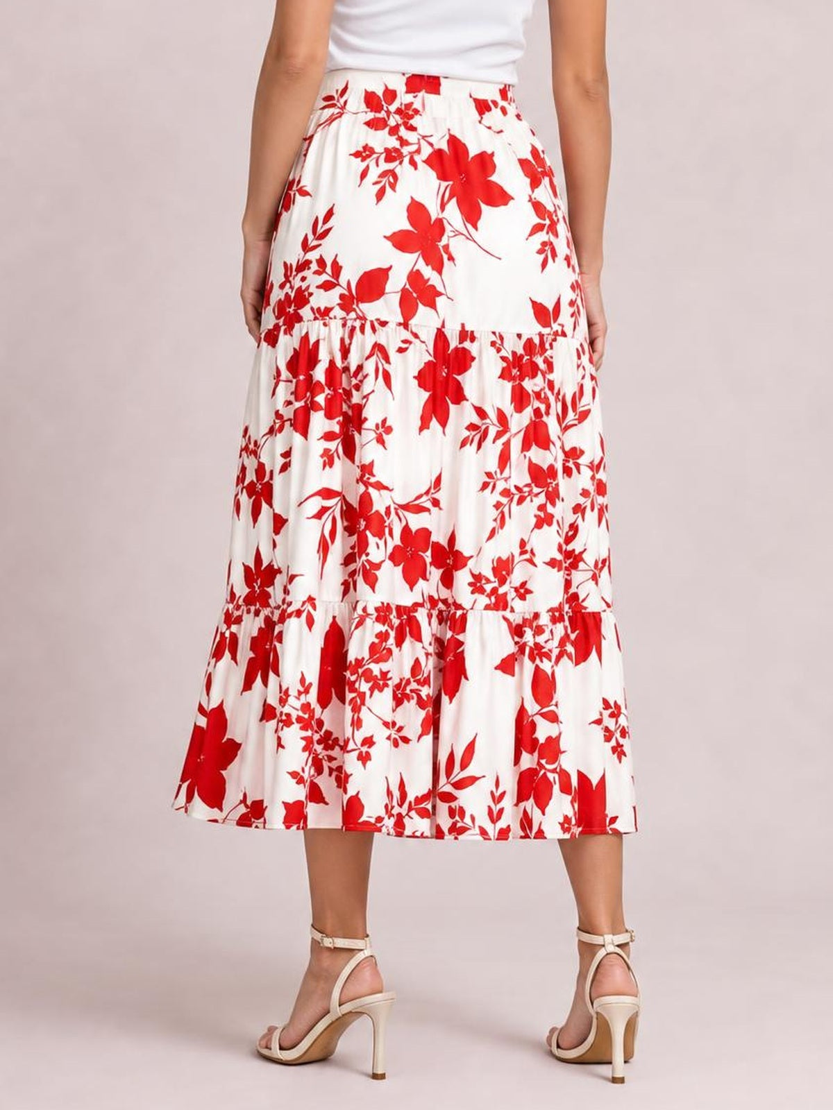 A model stands with hands at her sides wearing a flowy white midi skirt with a bold red floral print, tiered construction, and ruffled hem.