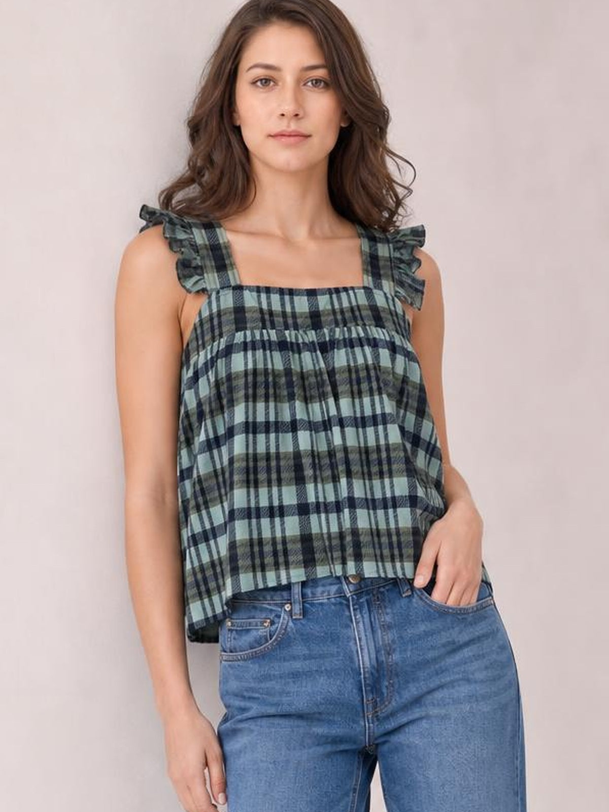 Model poses in a green and navy plaid tank with a square neckline, ruffled shoulder straps, and a relaxed, slightly flared silhouette.