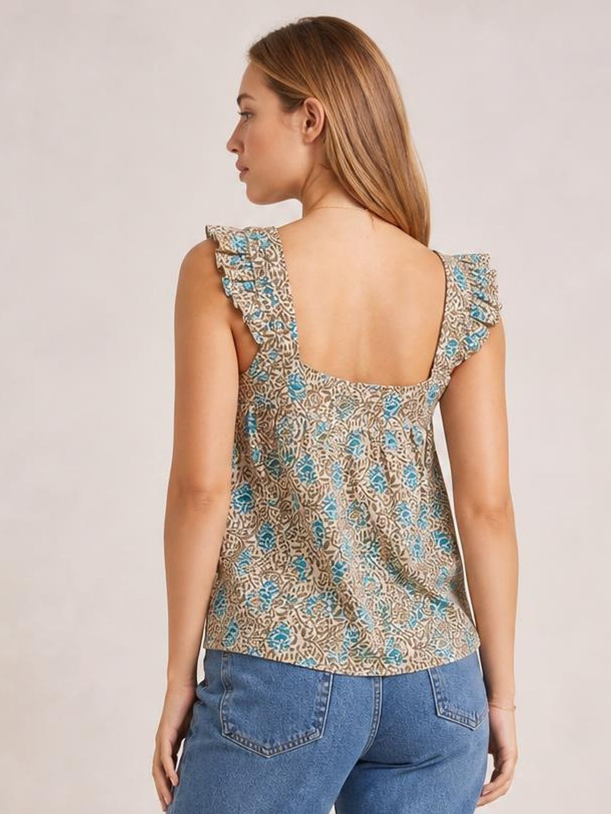 A model poses from the back in a beige, blue, and brown printed tank with ruffled straps, a square neckline, and a gently flared silhouette.