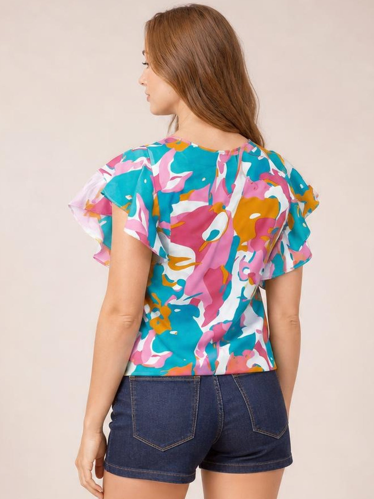 Model shown from behind wearing a colorful printed blouse with ruffled cap sleeves, a notched neckline, and a relaxed straight silhouette.