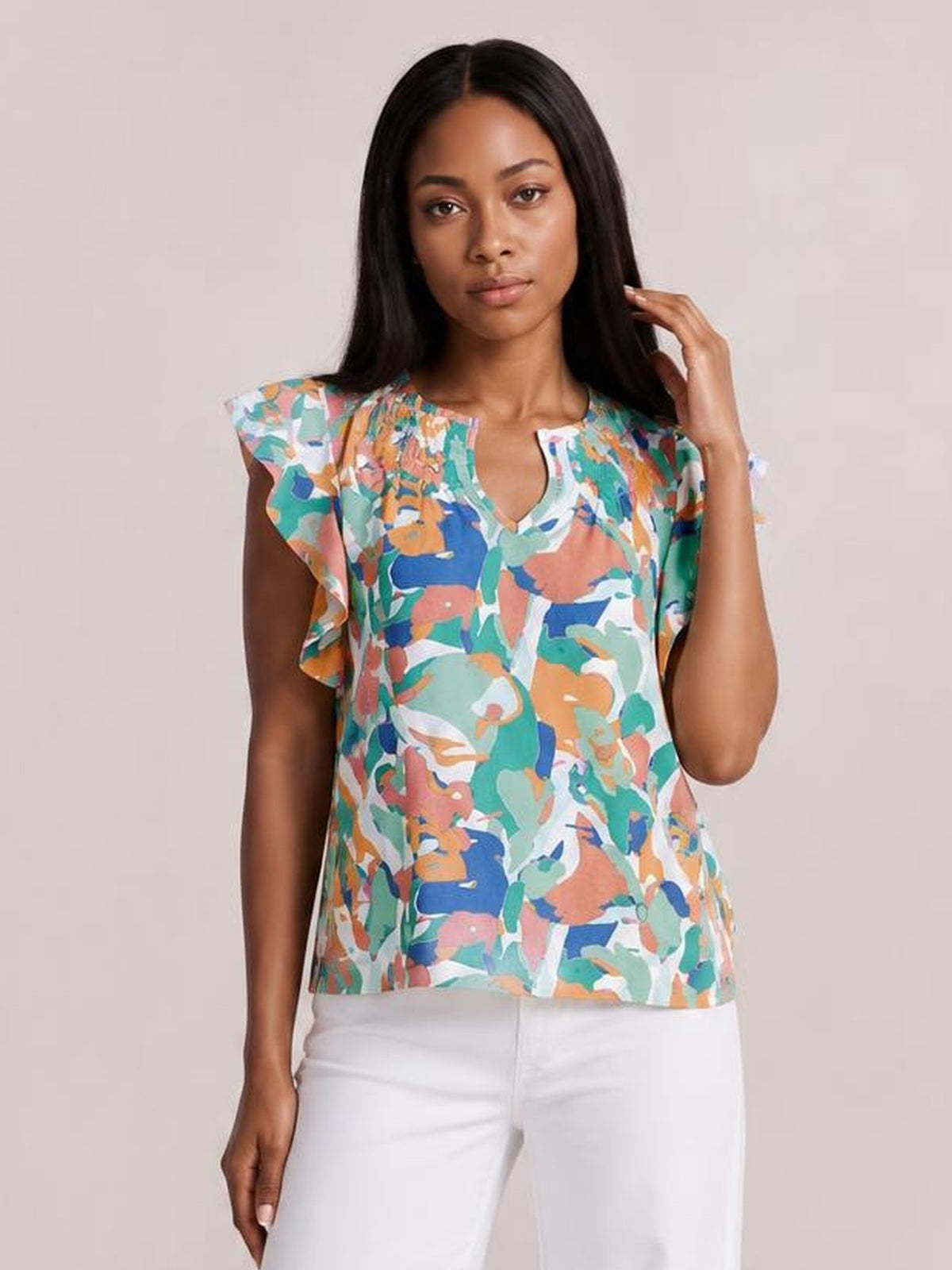 Model wearing a colorful printed blouse with ruffled cap sleeves, a notched neckline, and a relaxed straight silhouette, posing with one hand near her hair.