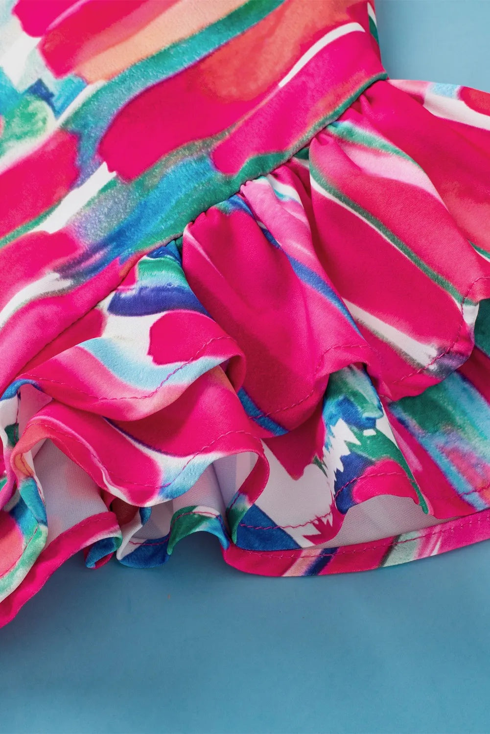 Close-up of a vibrant pink printed blouse with teal, blue, and white accents, showing layered ruffles and neatly finished seams.