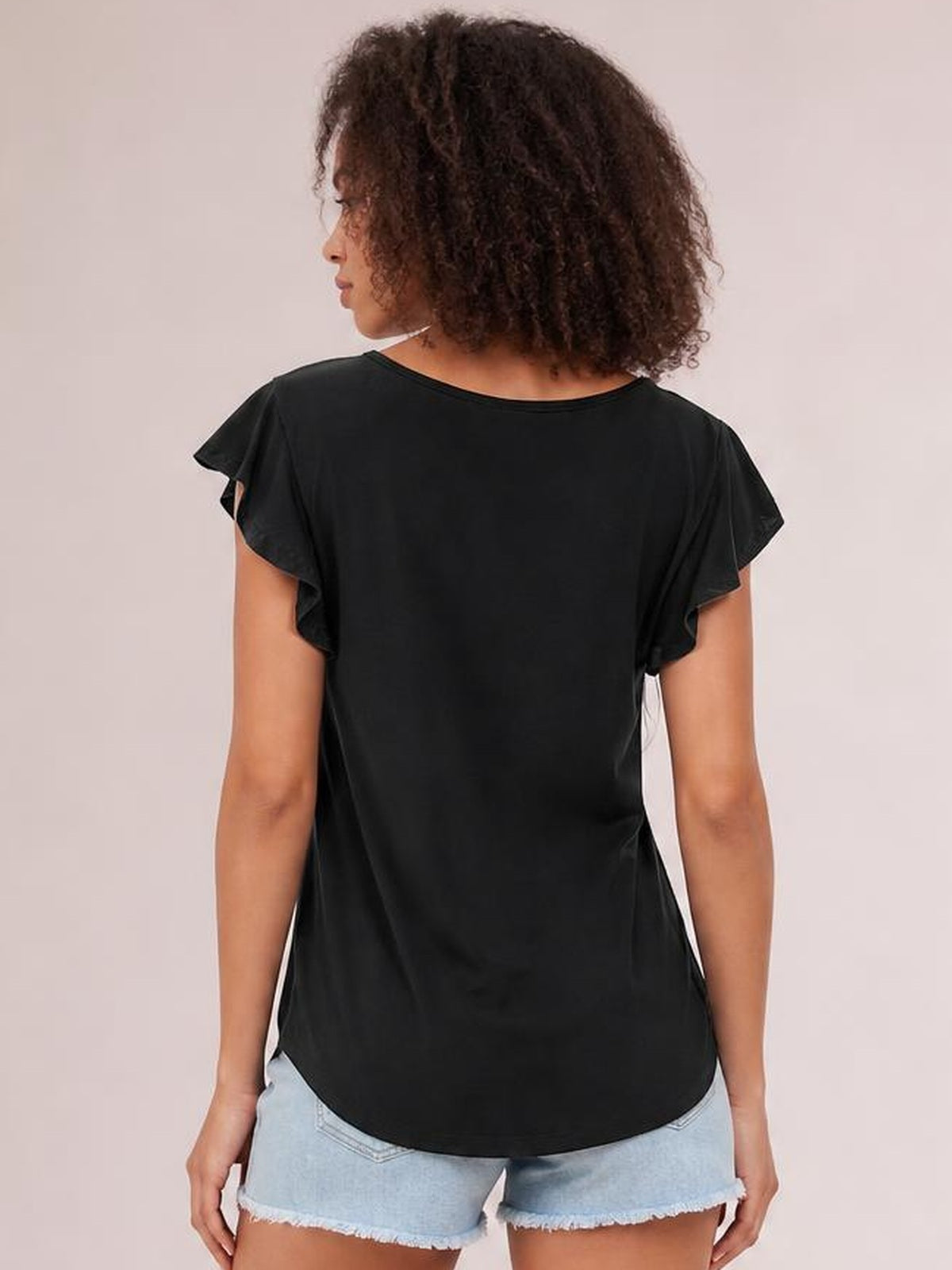 A model stands facing away in a black ruffled round-neck cap-sleeve blouse with a relaxed silhouette and curved hem.