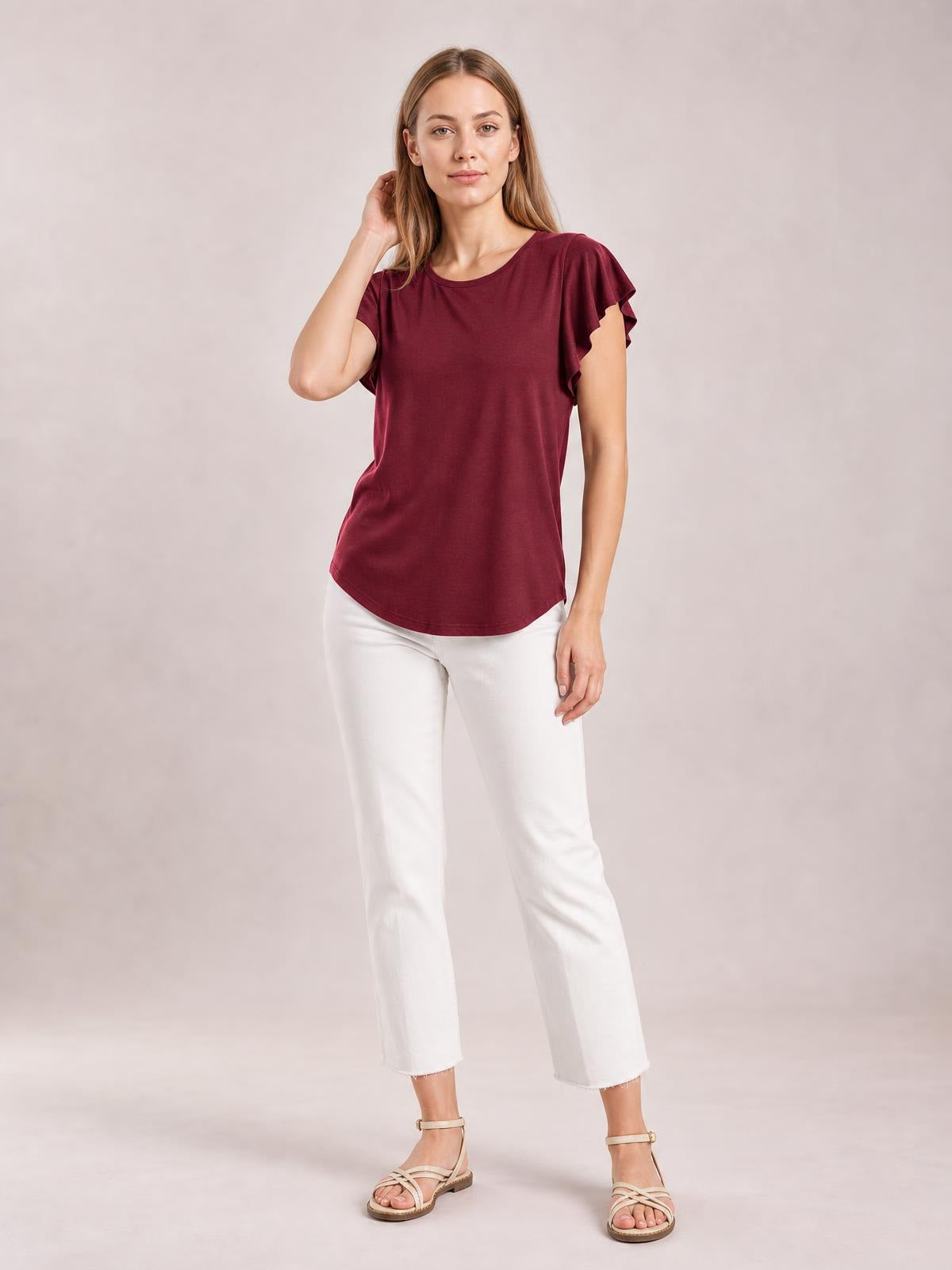 A model poses in a burgundy ruffled round-neck blouse with cap sleeves, a relaxed straight silhouette, and a gently curved hem.