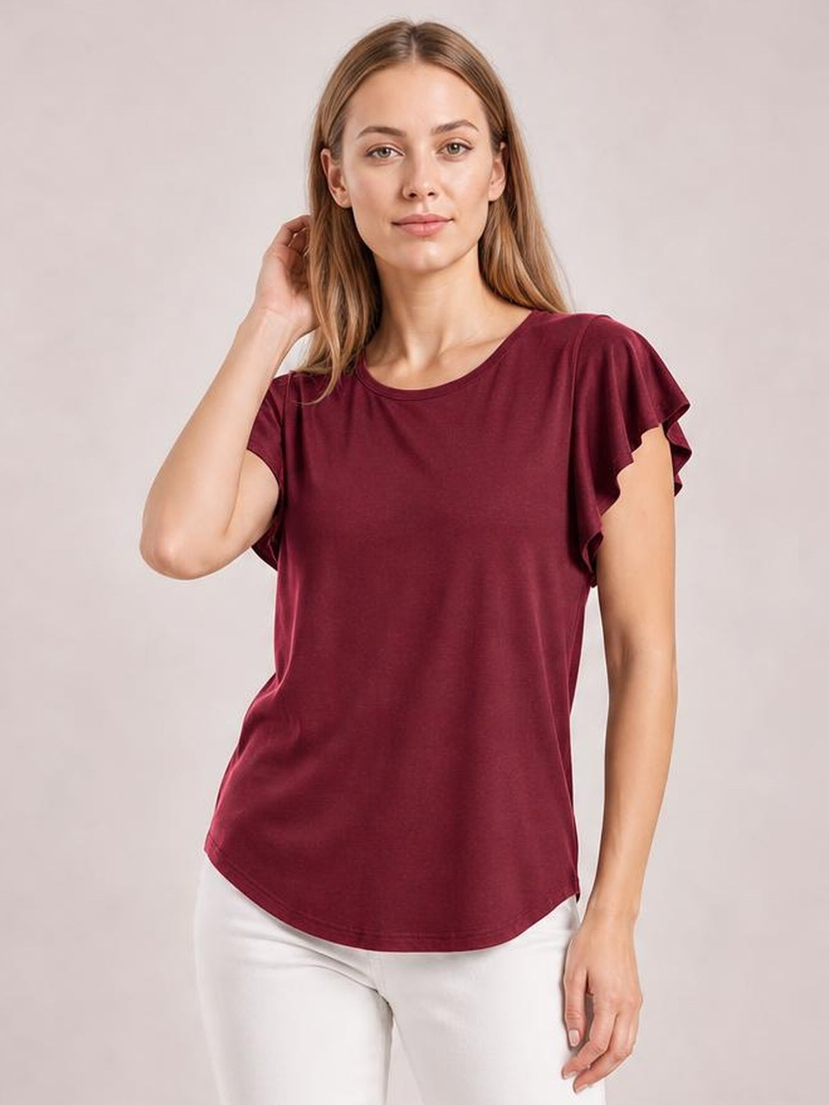 Model wears a burgundy ruffled round-neck blouse with layered cap sleeves, a relaxed straight silhouette, and a curved hem while touching her hair.