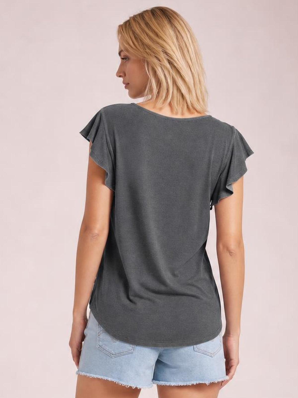 Model shown from the back wearing a charcoal gray ruffled round neck cap sleeve blouse with a relaxed silhouette and curved hem.