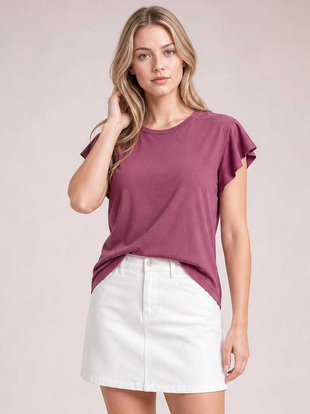 Model poses with one hand in her hair wearing a burgundy ruffled round-neck blouse with cap sleeves and a relaxed, slightly loose silhouette.