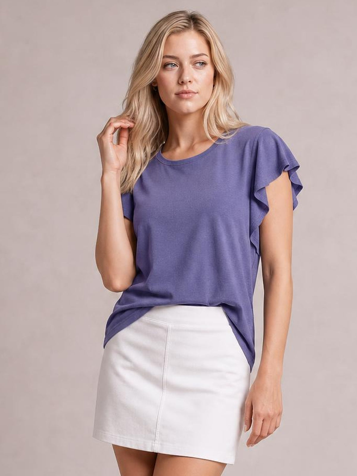 Model wearing a purple ruffled round neck cap sleeve blouse with a relaxed silhouette and curved hem, posing with one hand touching her hair.