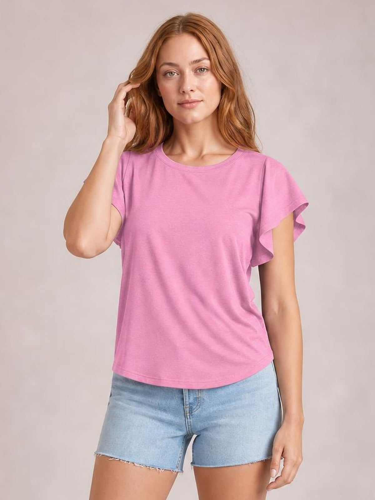 Model wearing a pink ruffled round neck cap sleeve blouse with a relaxed straight silhouette, posing with one hand touching her hair.