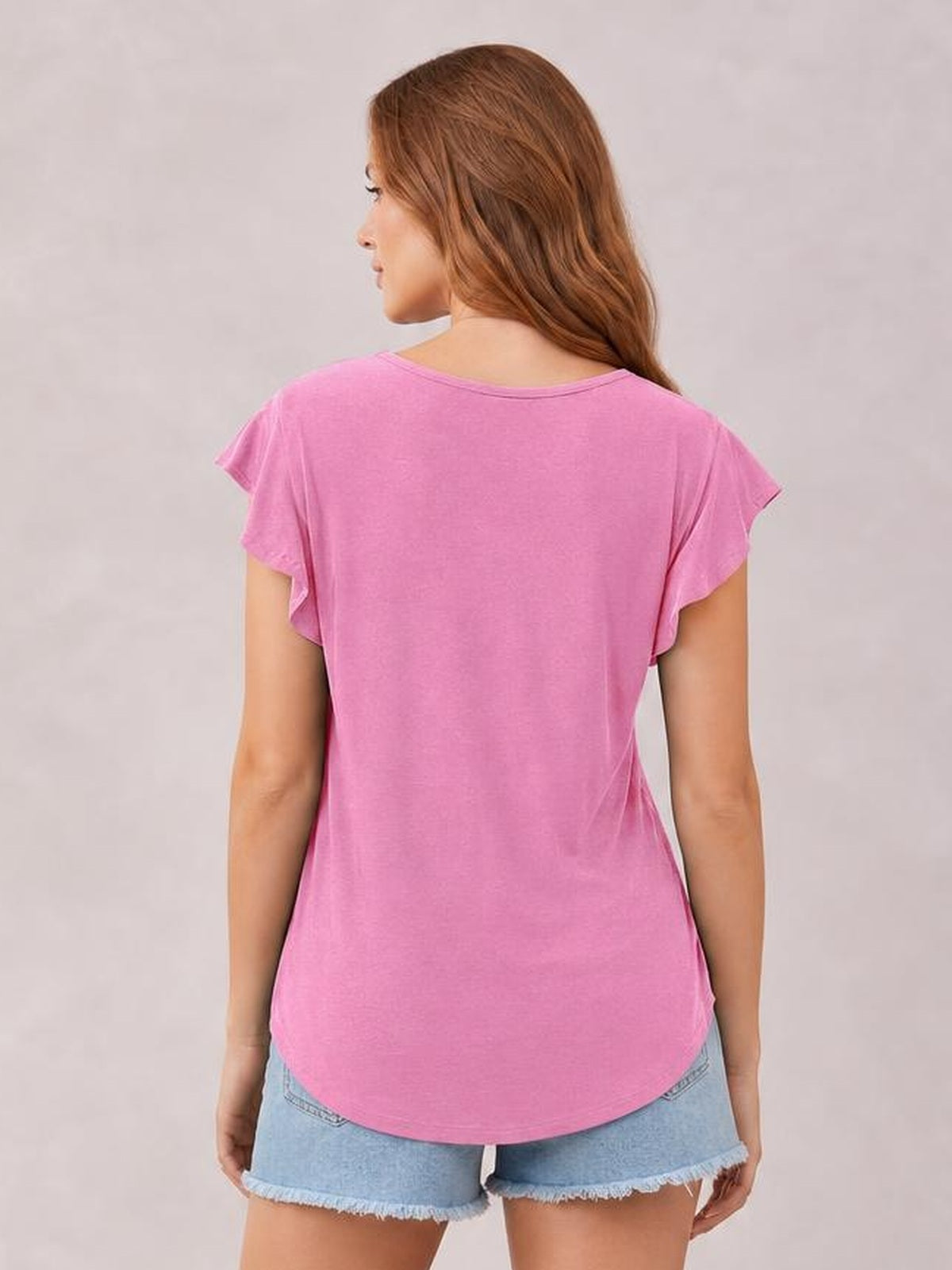 Back view of a model wearing a pink ruffled round neck cap sleeve blouse with a relaxed silhouette, curved hem, and lightly flounced sleeve edges.