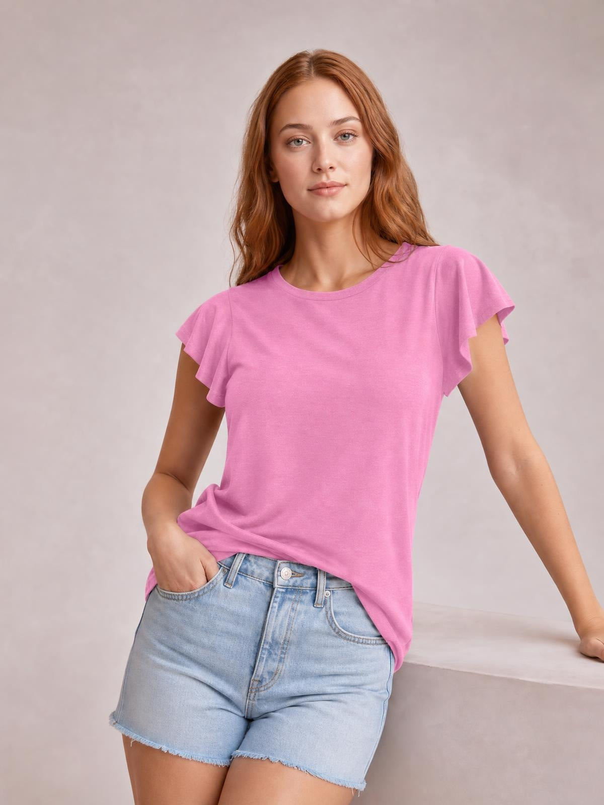 Model wearing a pink ruffled round-neck cap-sleeve blouse with a relaxed straight silhouette, posing with one hand in her denim shorts pocket.