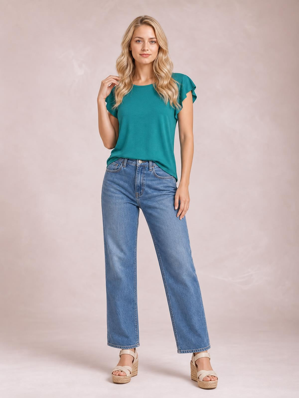 A model poses in a teal ruffled round neck cap sleeve blouse with a relaxed straight silhouette and layered sleeve construction.