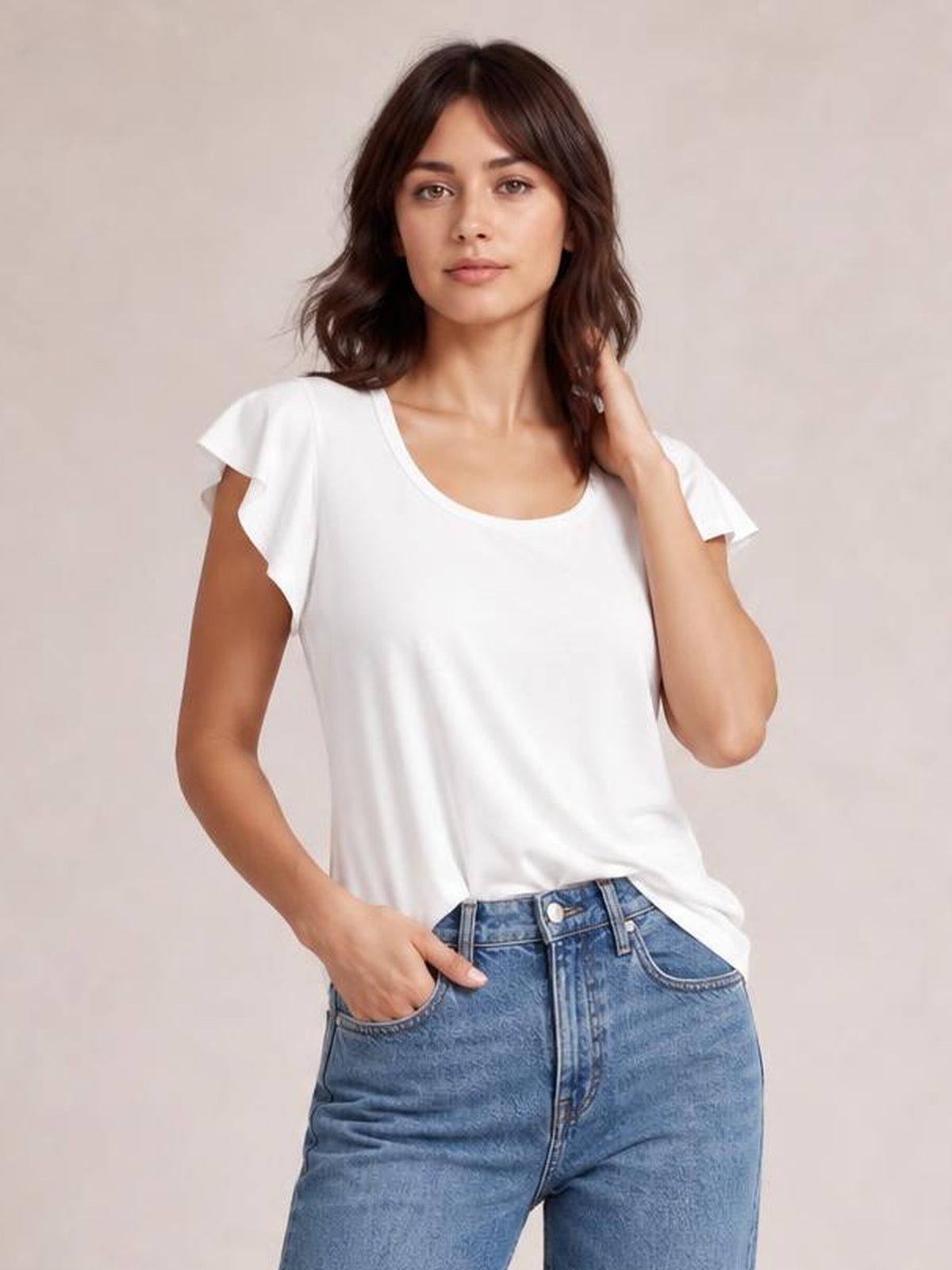 Model wearing a white ruffled round neck cap sleeve blouse with a relaxed straight silhouette, posing with one hand in her jeans pocket.