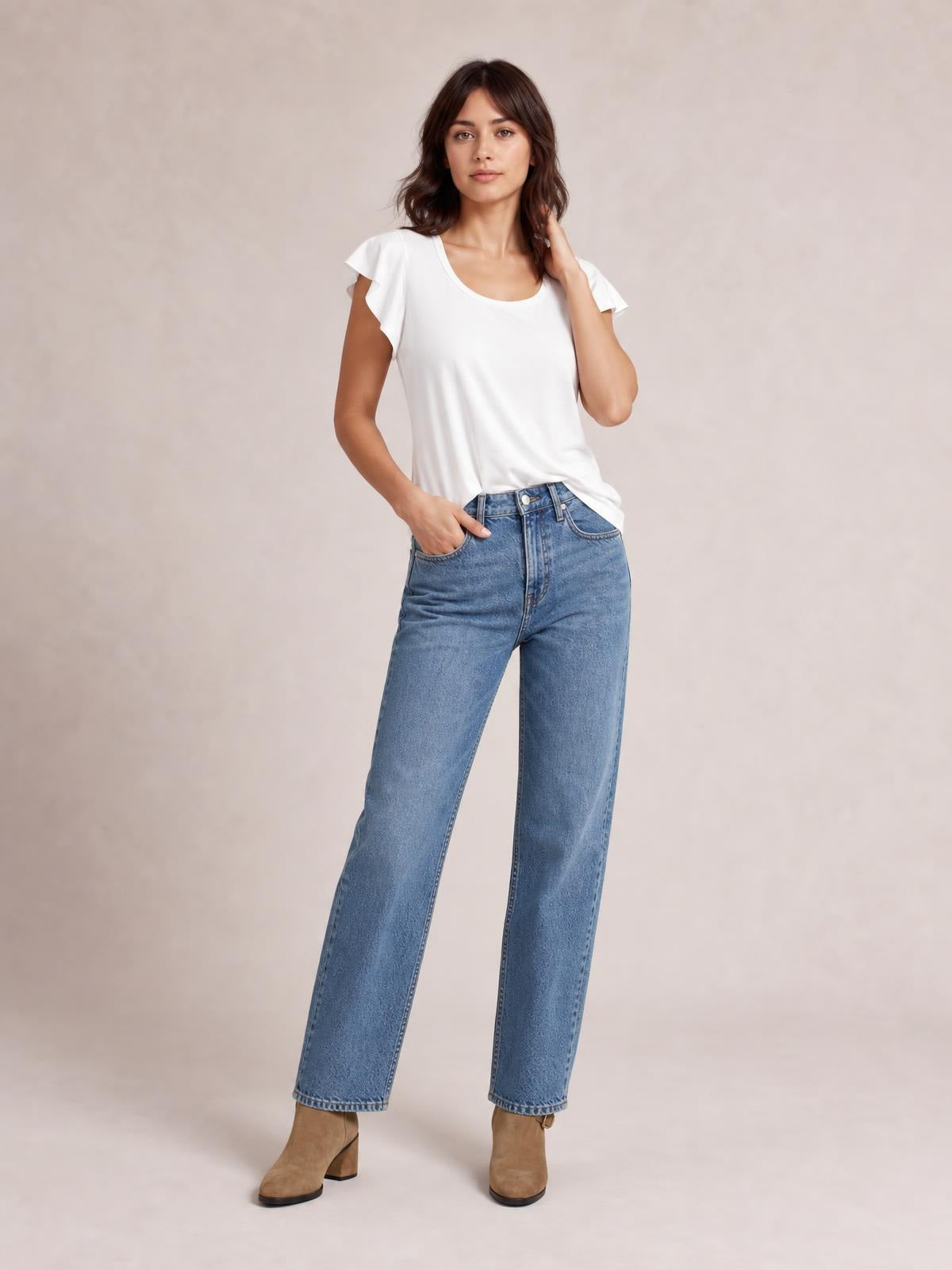 A model wears a white ruffled round-neck cap-sleeve blouse with a relaxed straight silhouette, standing with one hand in her jeans pocket.