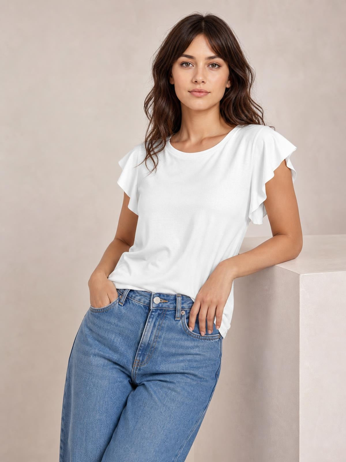Model poses in a white ruffled round neck cap sleeve blouse with a relaxed straight silhouette, paired with jeans and one hand in a pocket.