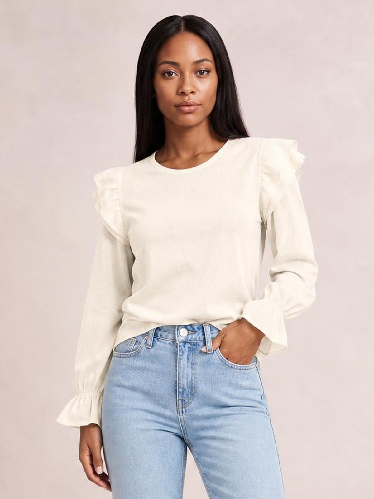 Model poses in a cream ruffled round-neck top with flounce sleeves, a relaxed straight silhouette, and gathered cuffs, paired with light-wash jeans.