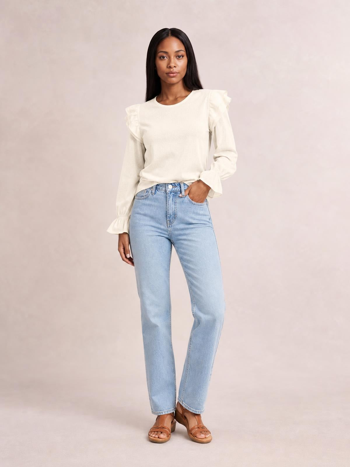 Model wears an ivory ruffled round neck top with flounce sleeves, gathered cuffs, and a relaxed straight silhouette, posing with one hand in her jeans pocket.
