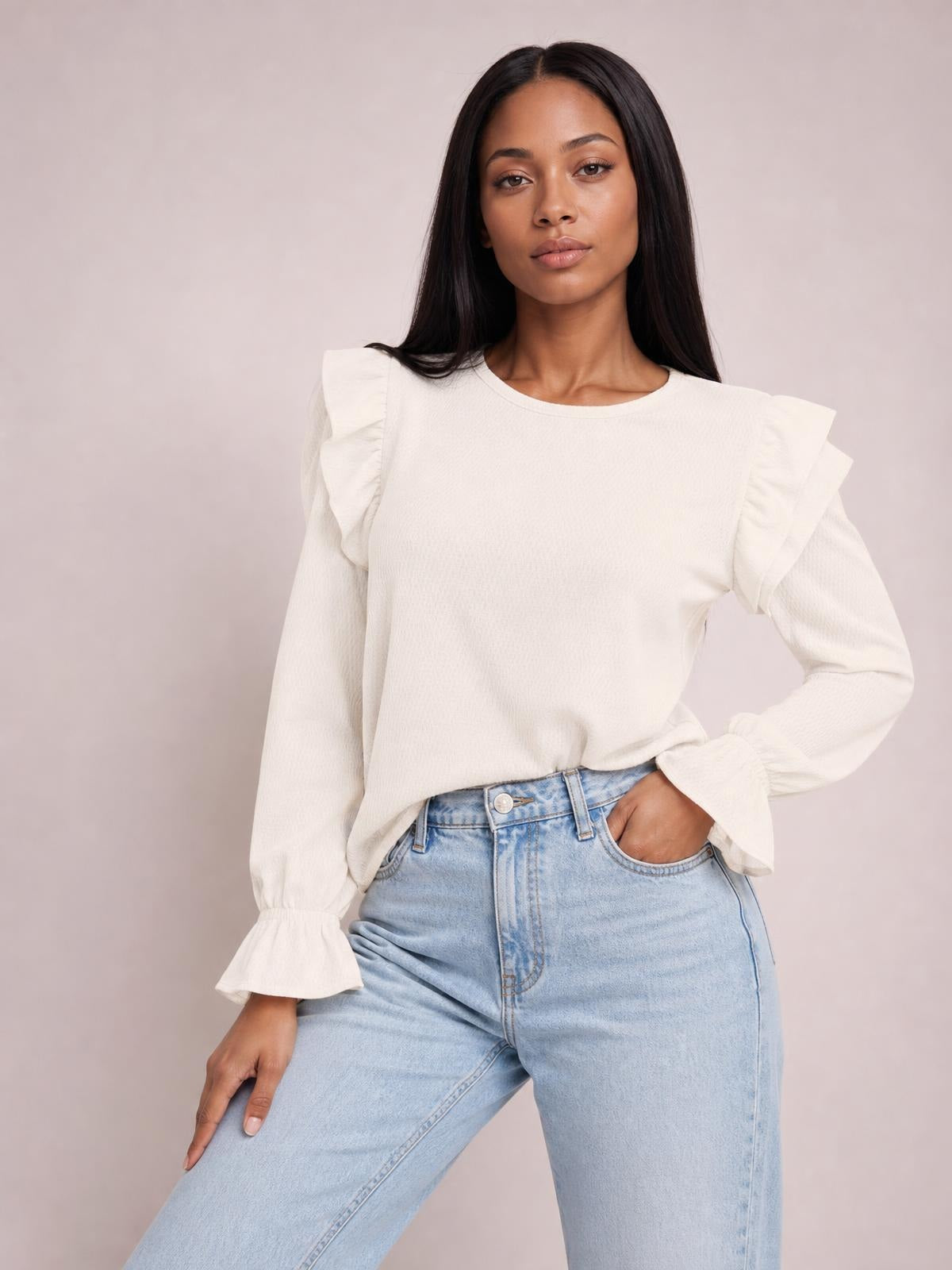 A model poses in a white ruffled top with a round neck, flounce sleeves, gathered cuffs, and a relaxed silhouette, standing with one hand in her jeans pocket.