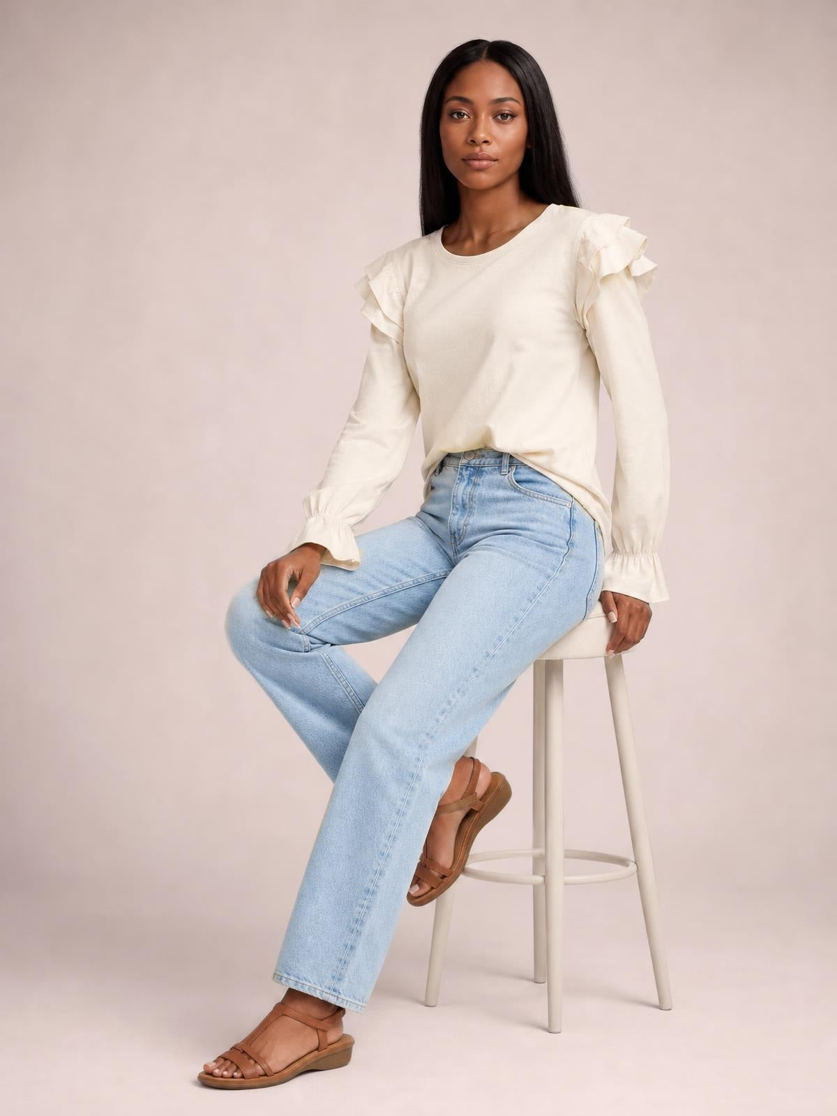 Model seated in a relaxed pose wearing an ivory round-neck top with layered ruffled flounce sleeves and gathered cuffs.
