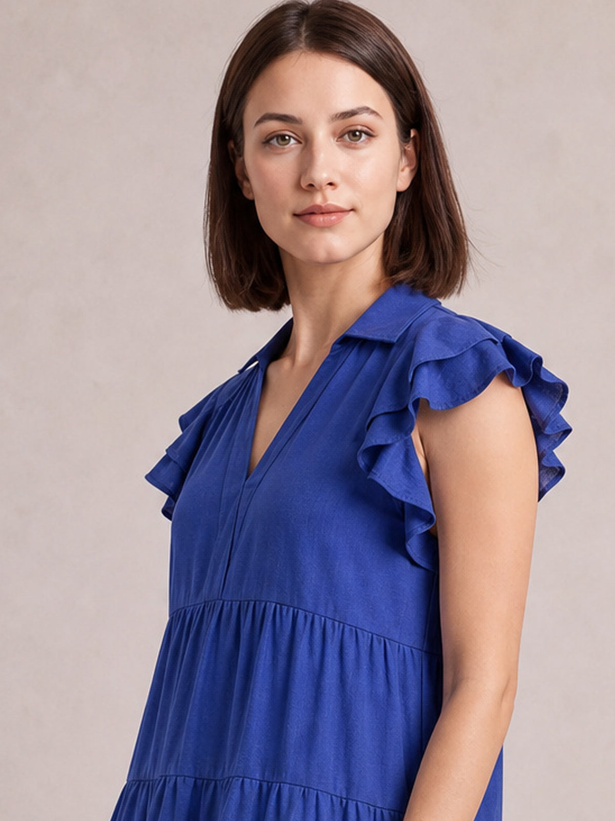 A model faces forward in a light indigo tiered midi dress with a collared V-neck, gathered seams, and softly ruffled short sleeves.
