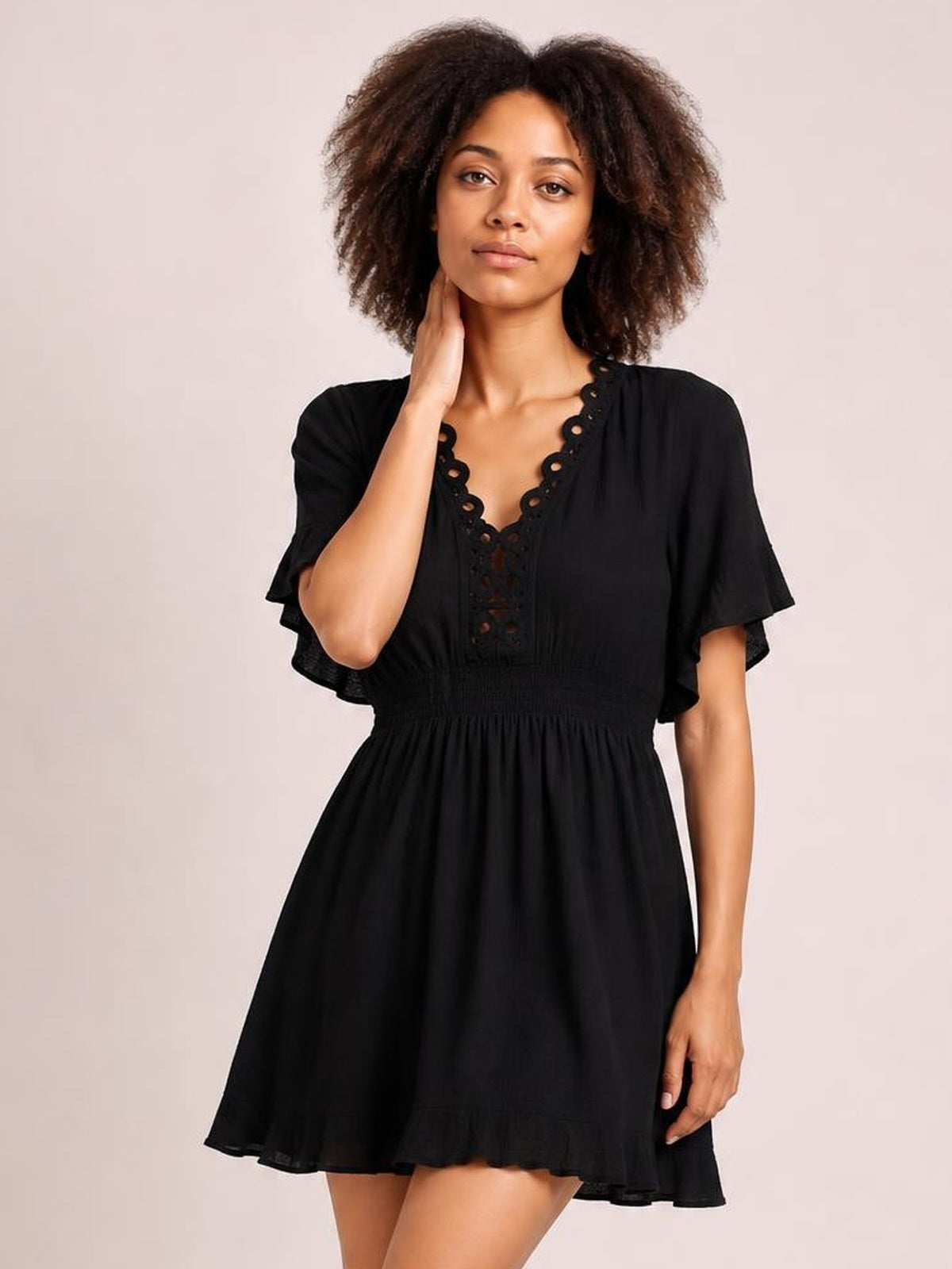 A model poses in a black V-neck cover-up with cutout trim, ruffled short sleeves and hem, a smocked waist, and a flared silhouette.