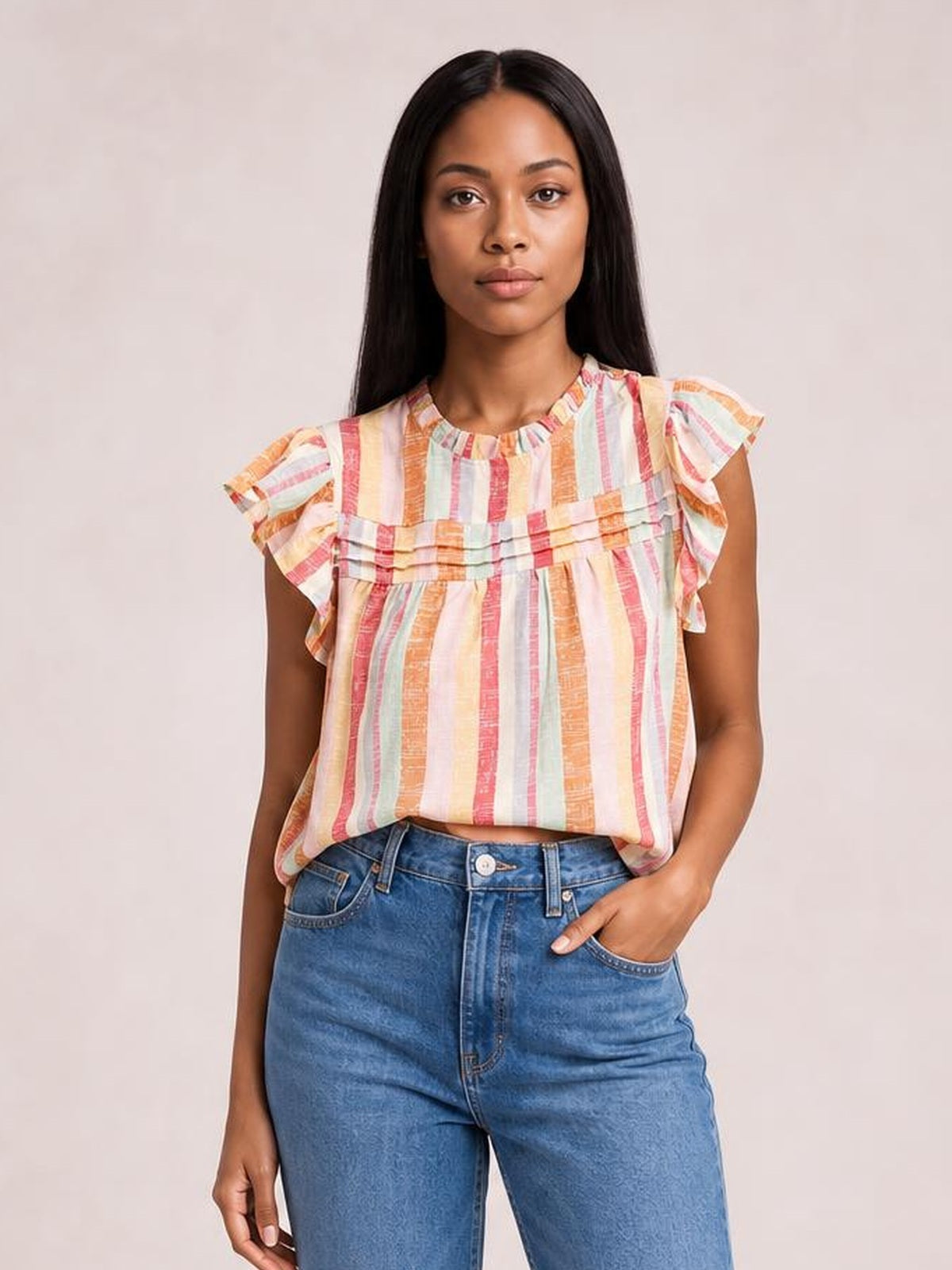 Model wearing a multicolor striped round neck blouse with layered ruffles, fluttering cap sleeves, and a loose straight silhouette, one hand in her jeans pocket.