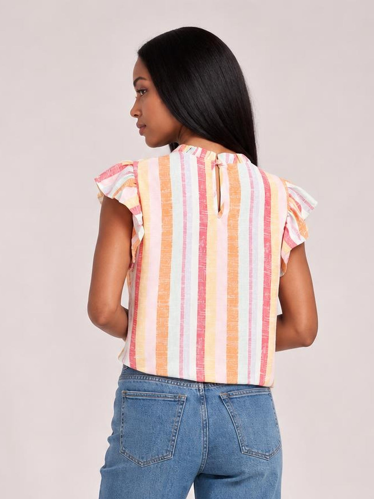 A model wears a pastel striped blouse with ruffled cap sleeves and a round neckline, shown from the back in a relaxed pose with a straight silhouette.