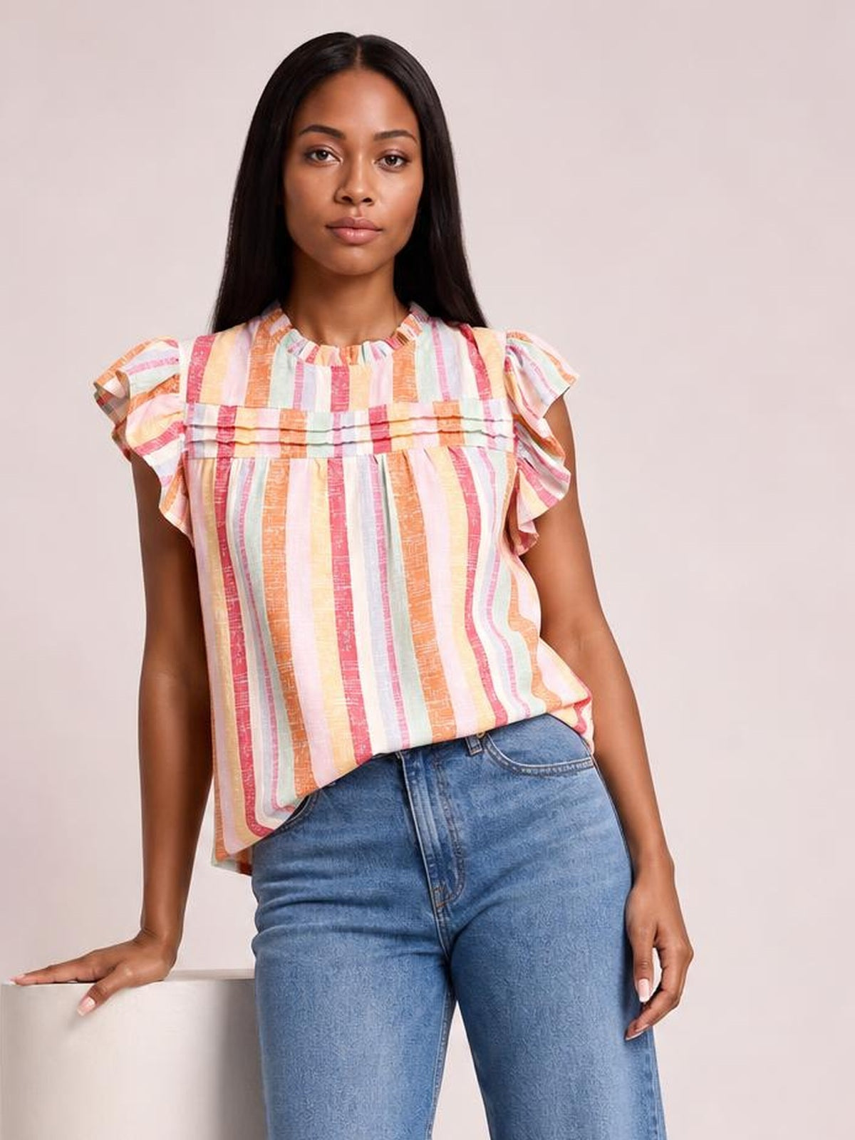 Model poses in a colorful striped blouse with a round ruffled neckline, fluttering cap sleeves, horizontal ruffle trim, and a relaxed silhouette.