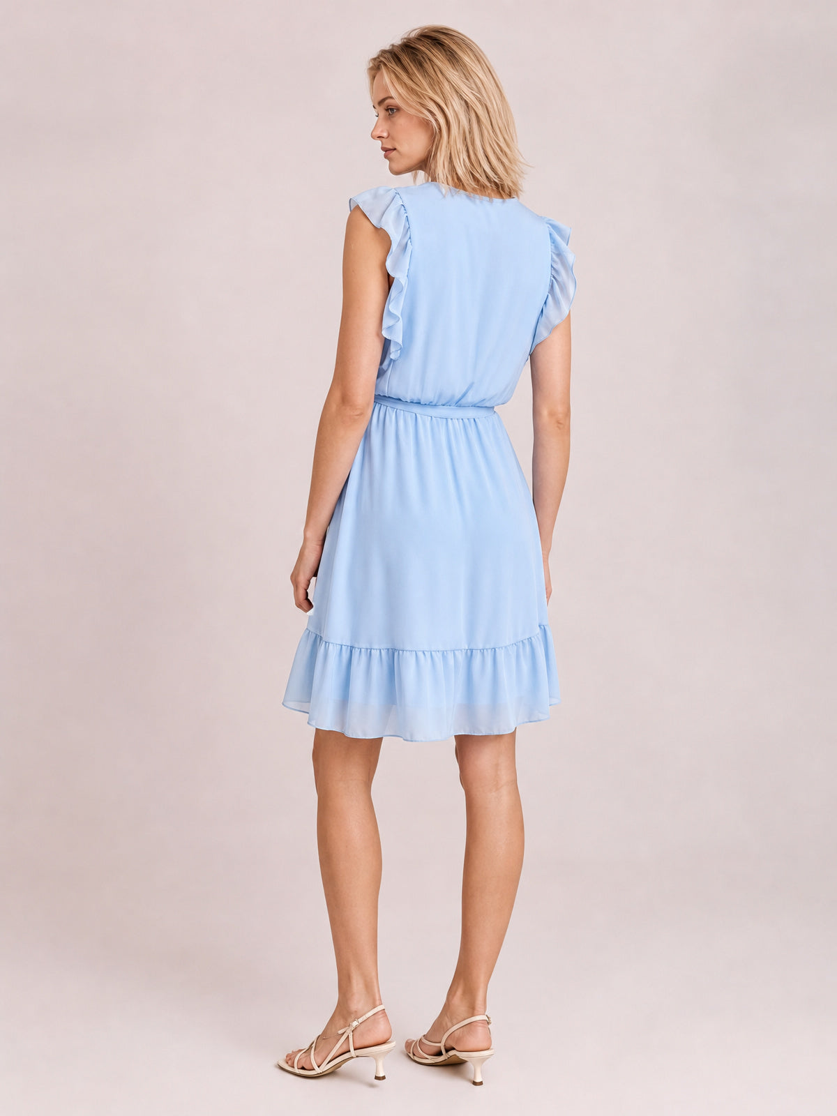 A model poses in a light blue ruffled cap sleeve dress, shown from the back with a defined waist, softly gathered skirt, and tiered ruffle hem.
