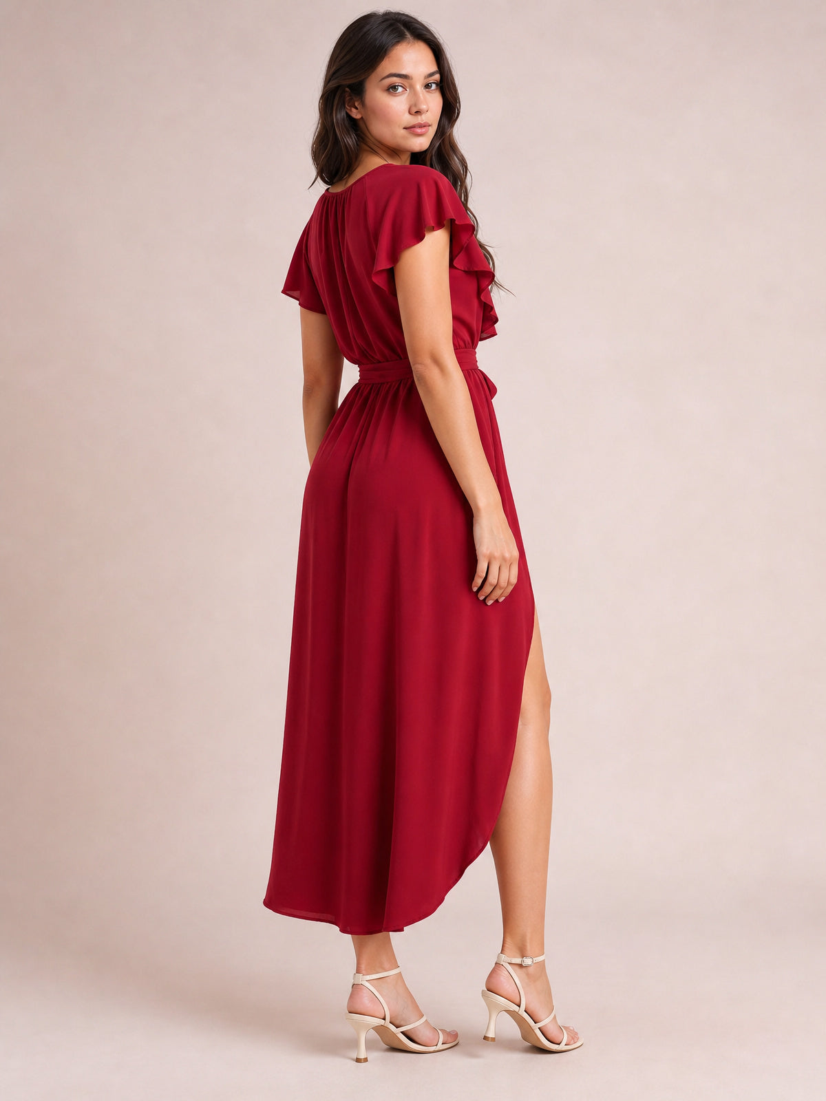 Model poses in a burgundy ruffled surplice midi dress with flutter sleeves, a tied waist, flowing silhouette, and high side slit.