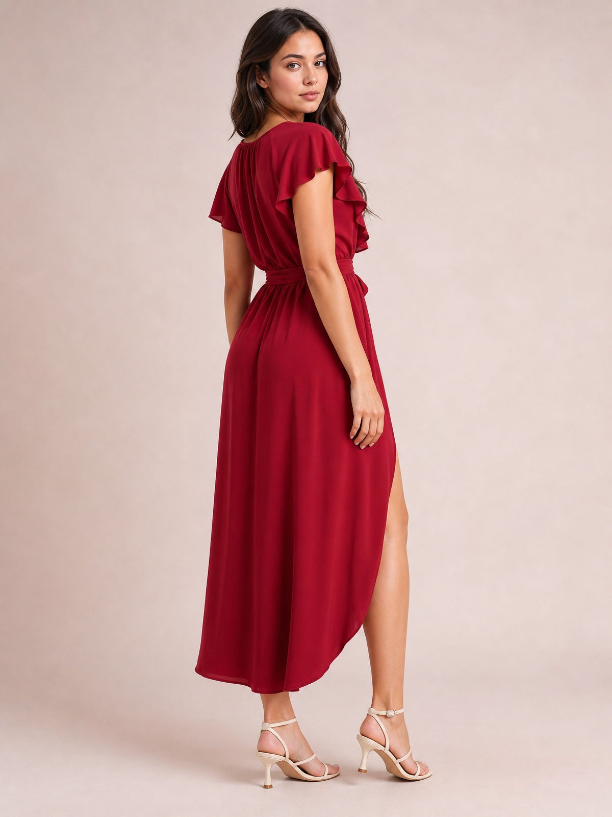 Model poses in a burgundy ruffled surplice midi dress with flutter sleeves, a tied waist, flowing silhouette, and high side slit.