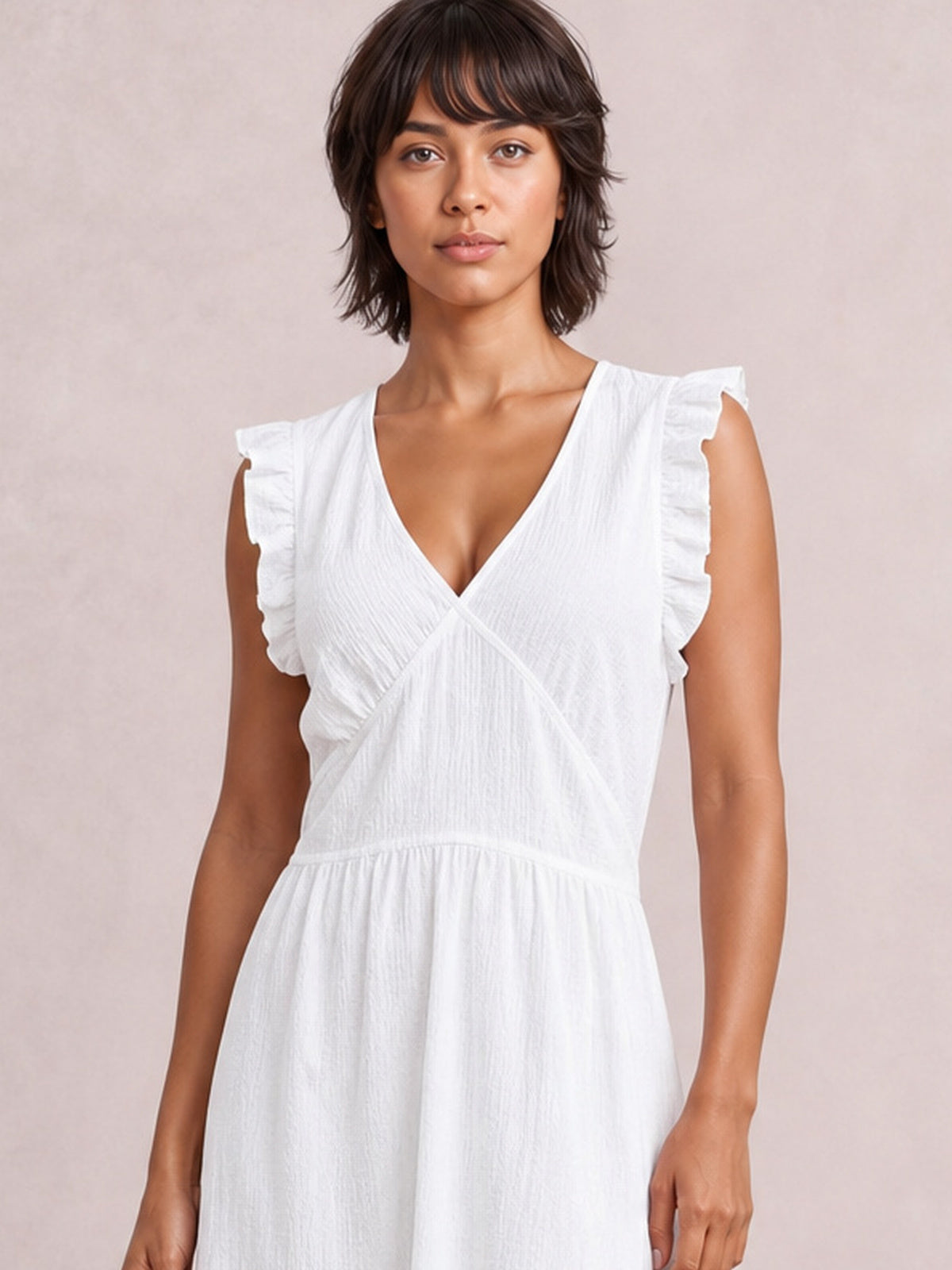 Model standing facing forward in a white ruffled V-neck maxi dress with cap sleeves, overlapping bodice panels, a gathered waist, and a flowing silhouette.
