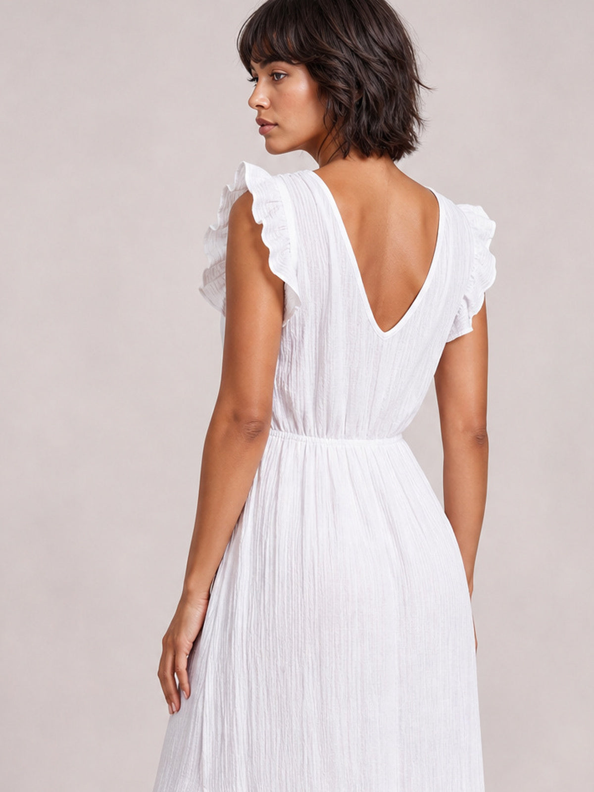 Model shown from the back in a white ruffled cap-sleeve maxi dress with a deep V-neckline, gathered waist, and flowing silhouette.