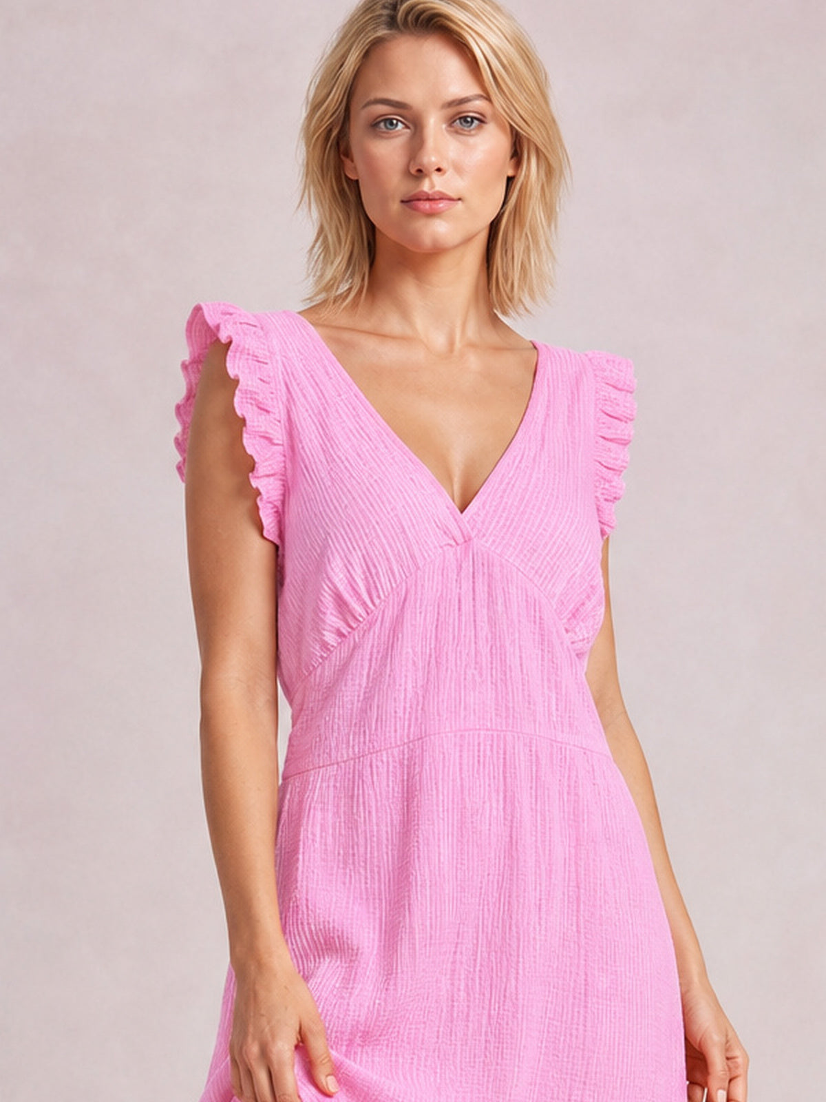 A model stands facing forward in a bright pink ruffled V-neck maxi dress with cap sleeves, gathered waist, flowing silhouette, and tiered skirt construction.