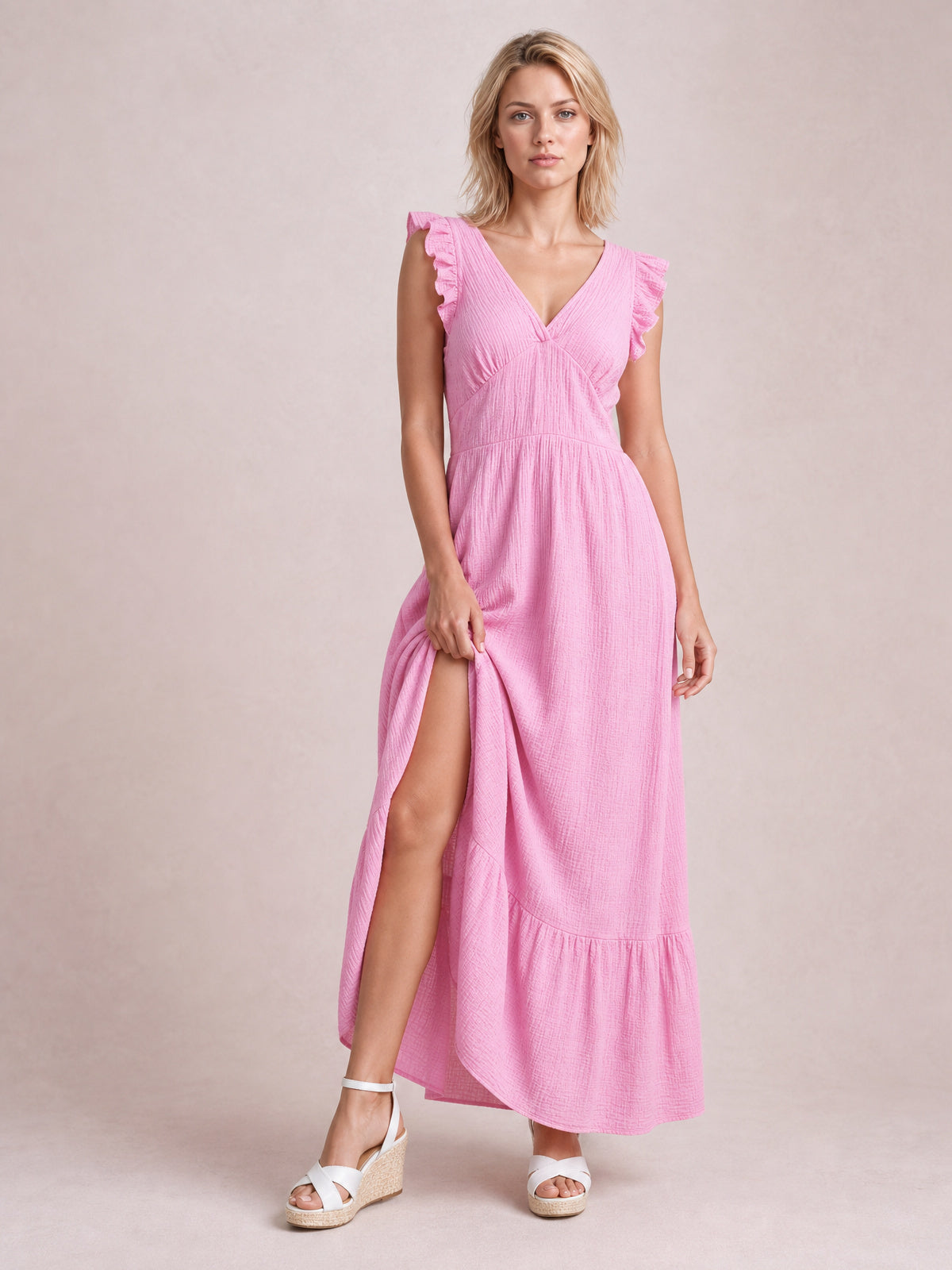 Model in a pink ruffled V-neck maxi dress with cap sleeves, a gathered waist, flowing tiered skirt, and visible side slit.