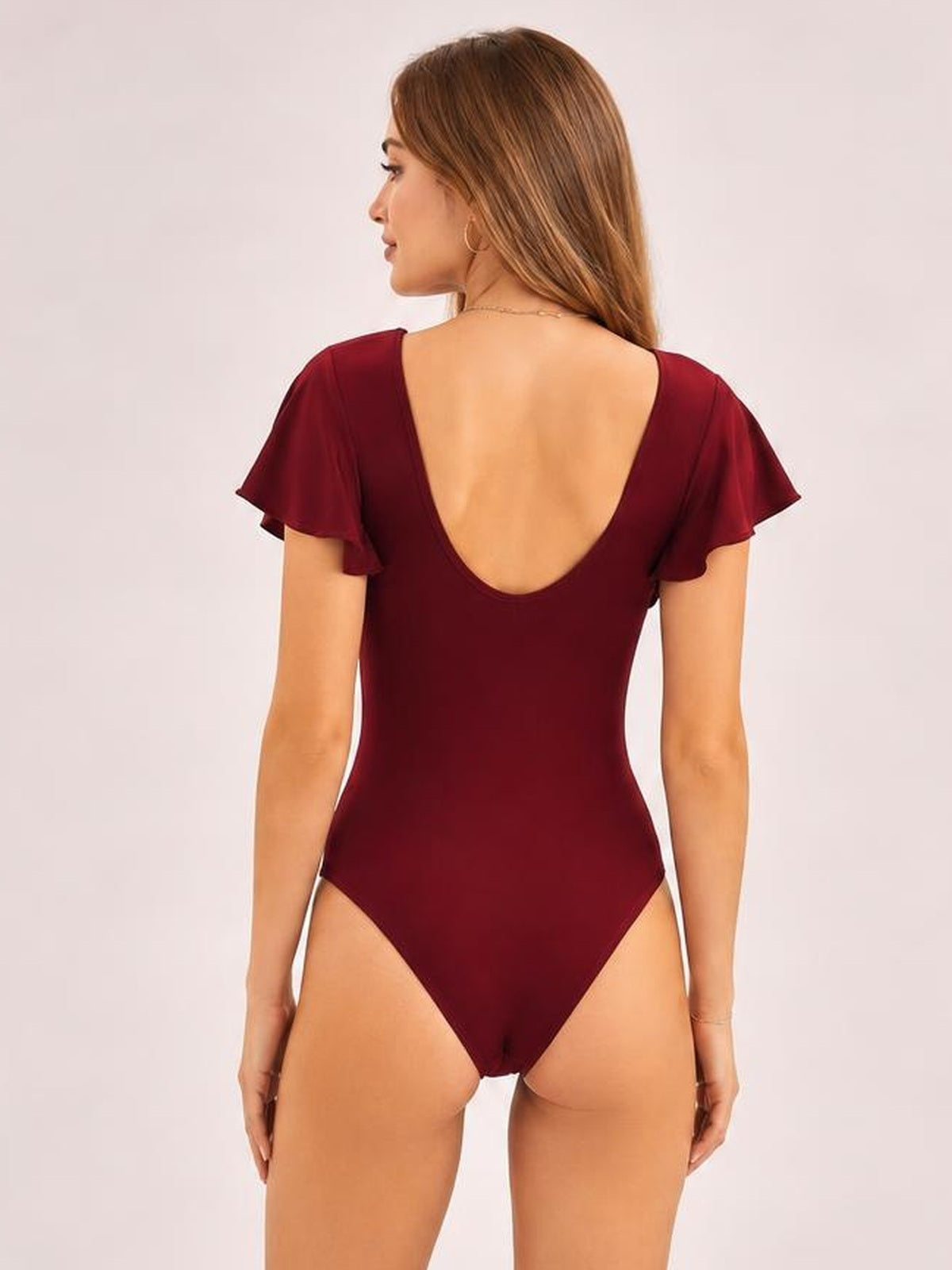 Model stands facing away in a burgundy one-piece swimsuit with ruffled cap sleeves, a deep scoop back, and a fitted silhouette.