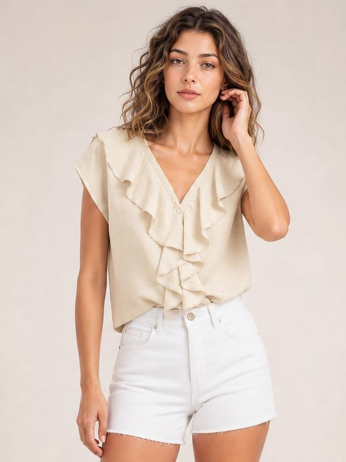 Model poses in a cream ruffled V-neck short sleeve blouse with a relaxed silhouette and layered front ruffle detail.