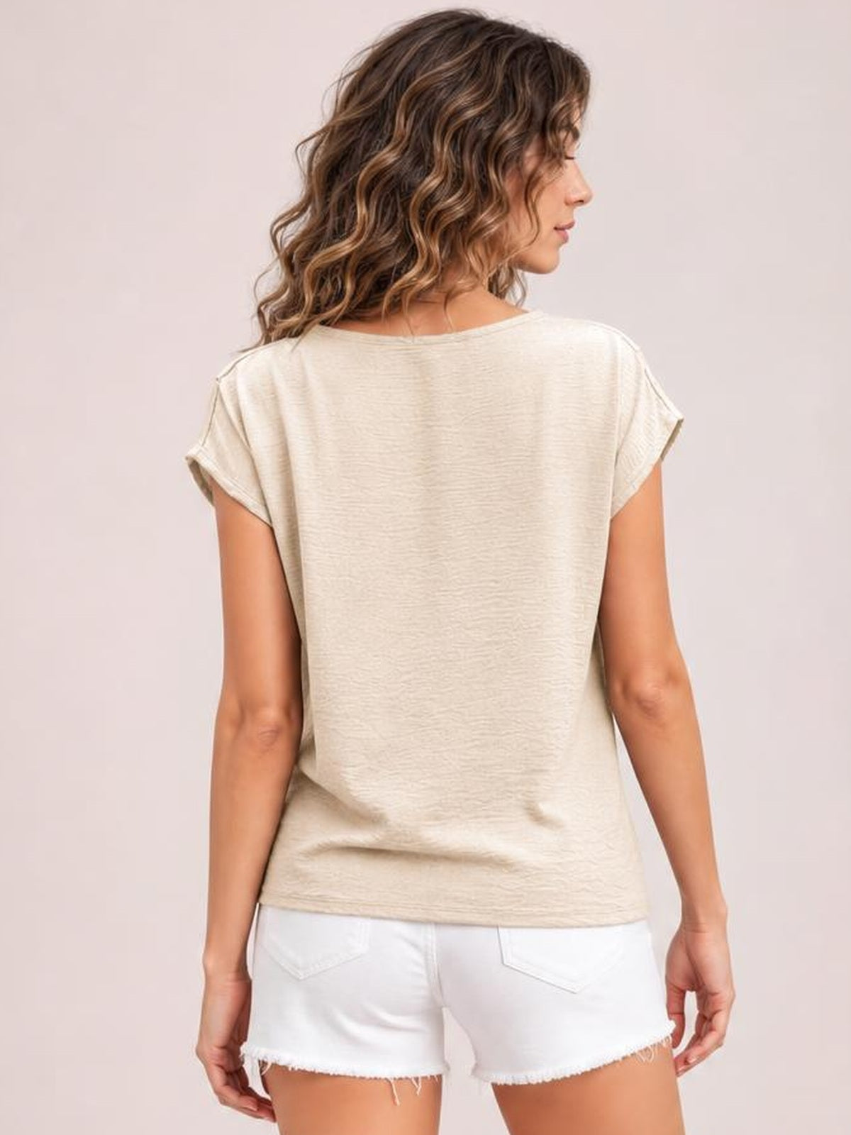 Back view of a model wearing an ivory short-sleeve blouse with a relaxed, straight silhouette, softly textured fabric, and rolled sleeve cuffs.