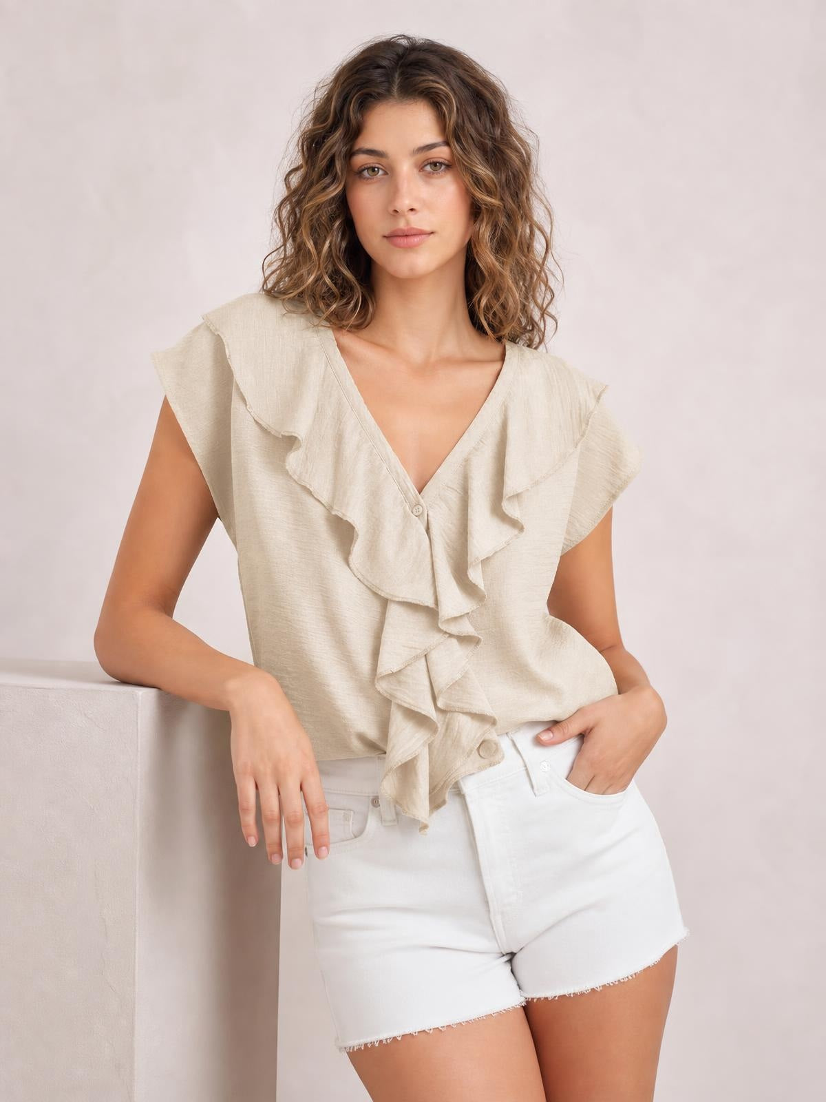 A model poses in a cream ruffled V-neck short-sleeve blouse with a relaxed silhouette, cascading front ruffles, and a button-front closure.
