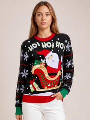A woman models a black Santa graphic round neck long sleeve sweater with a relaxed silhouette, snowflake motifs, and red and green ribbed cuffs and hem.