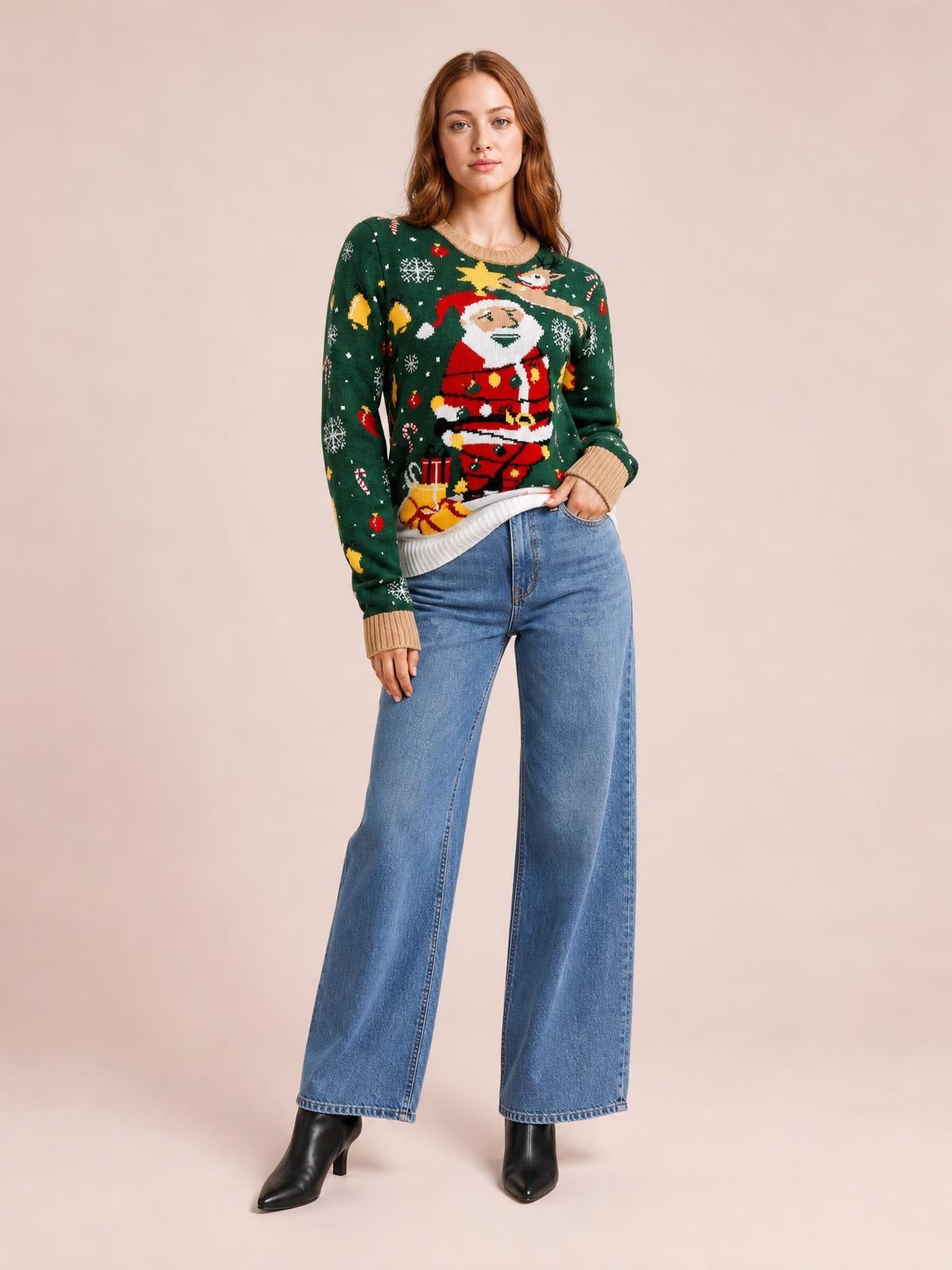 Model wearing a green Santa sweater with a round neck, long sleeves, ribbed beige trim, festive knit pattern, and relaxed silhouette, posing with one hand in her jeans pocket.