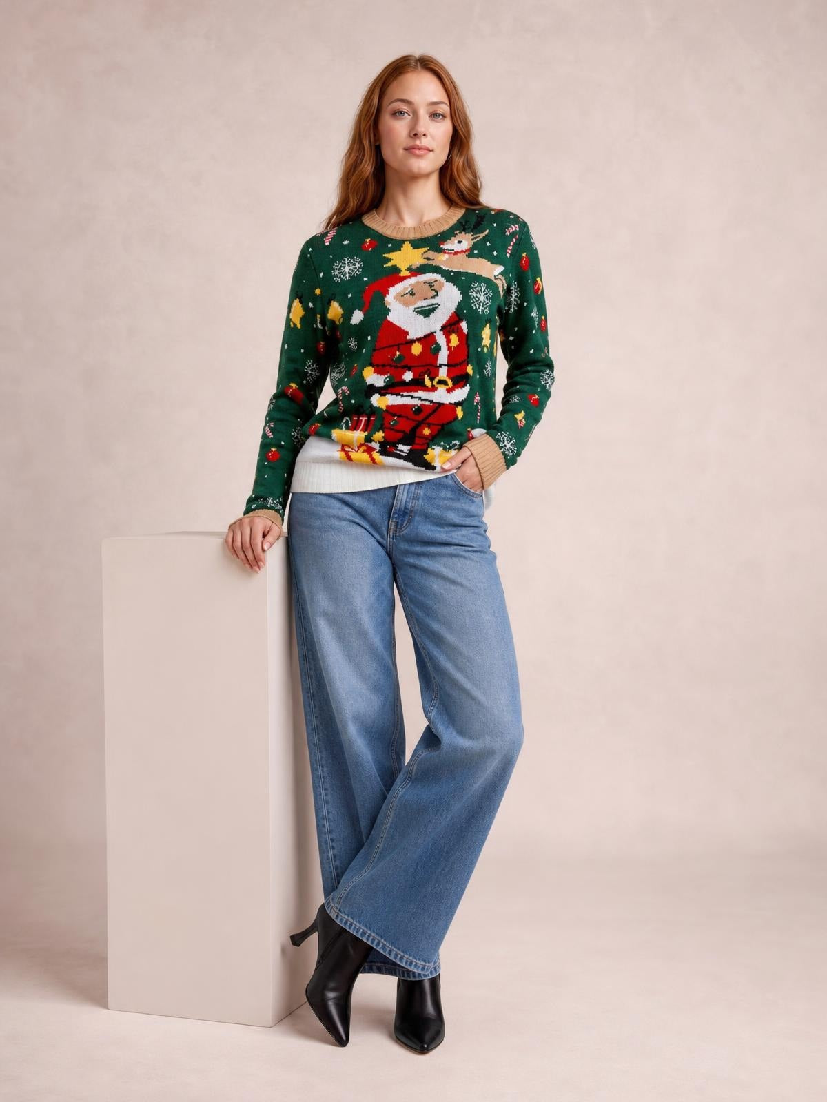 Model leans against a pedestal wearing a green Santa round-neck long-sleeve sweater with a relaxed silhouette, festive knit motif, and ribbed trim.