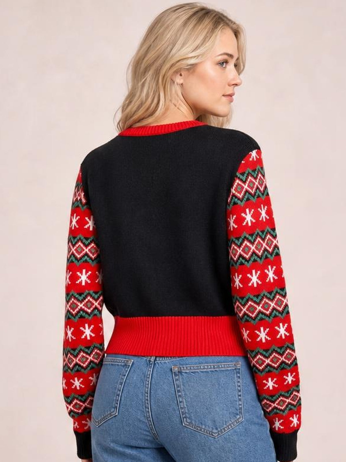 A model turns to show the back of a black long sleeve sweater with red, green, and white patterned sleeves, plus a ribbed red crew neck and hem.