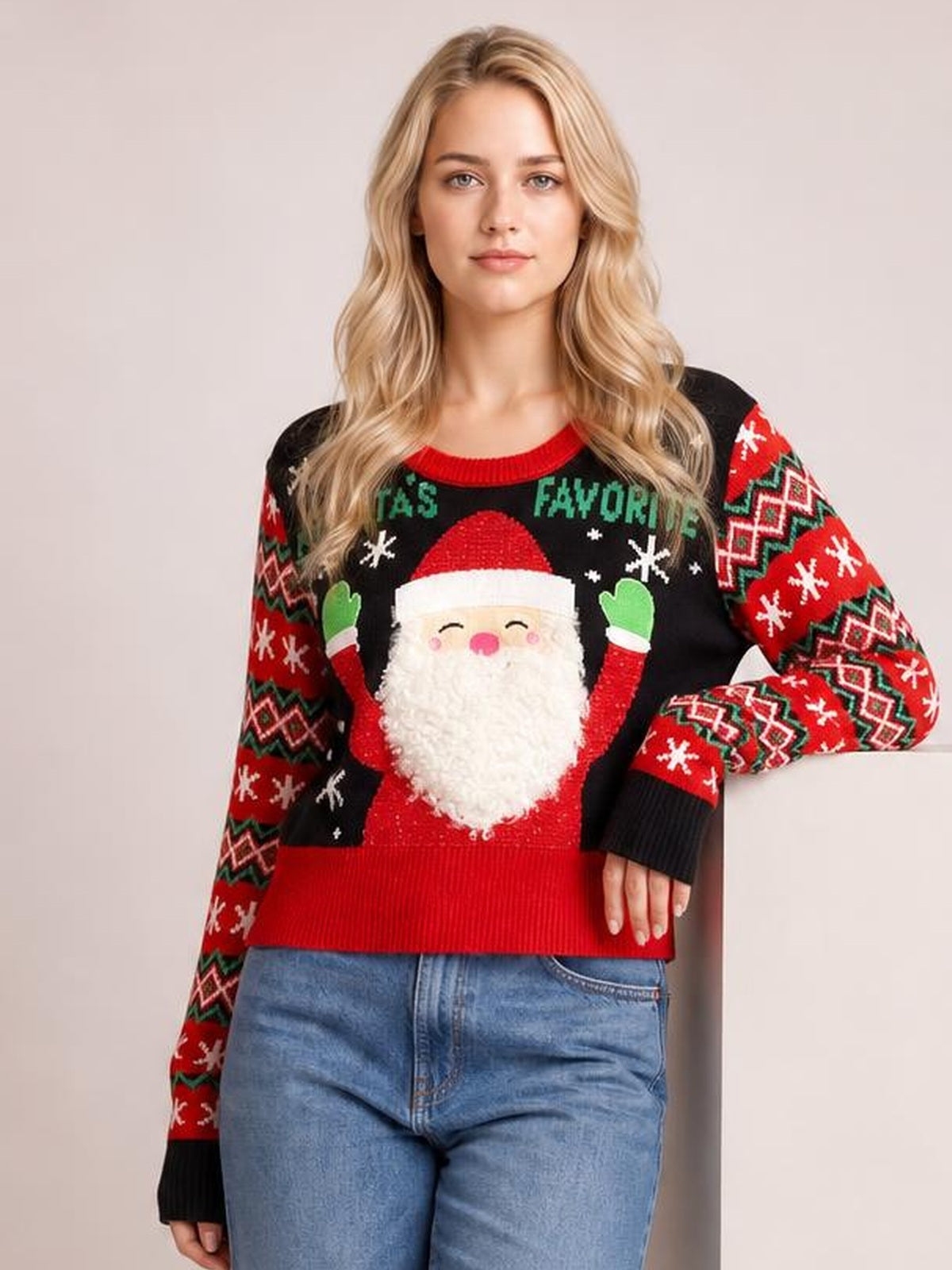 Model wearing a black SANTA’S FAVORITE graphic long sleeve sweater with a Santa design, red ribbed hem and cuffs, and festive patterned sleeves.