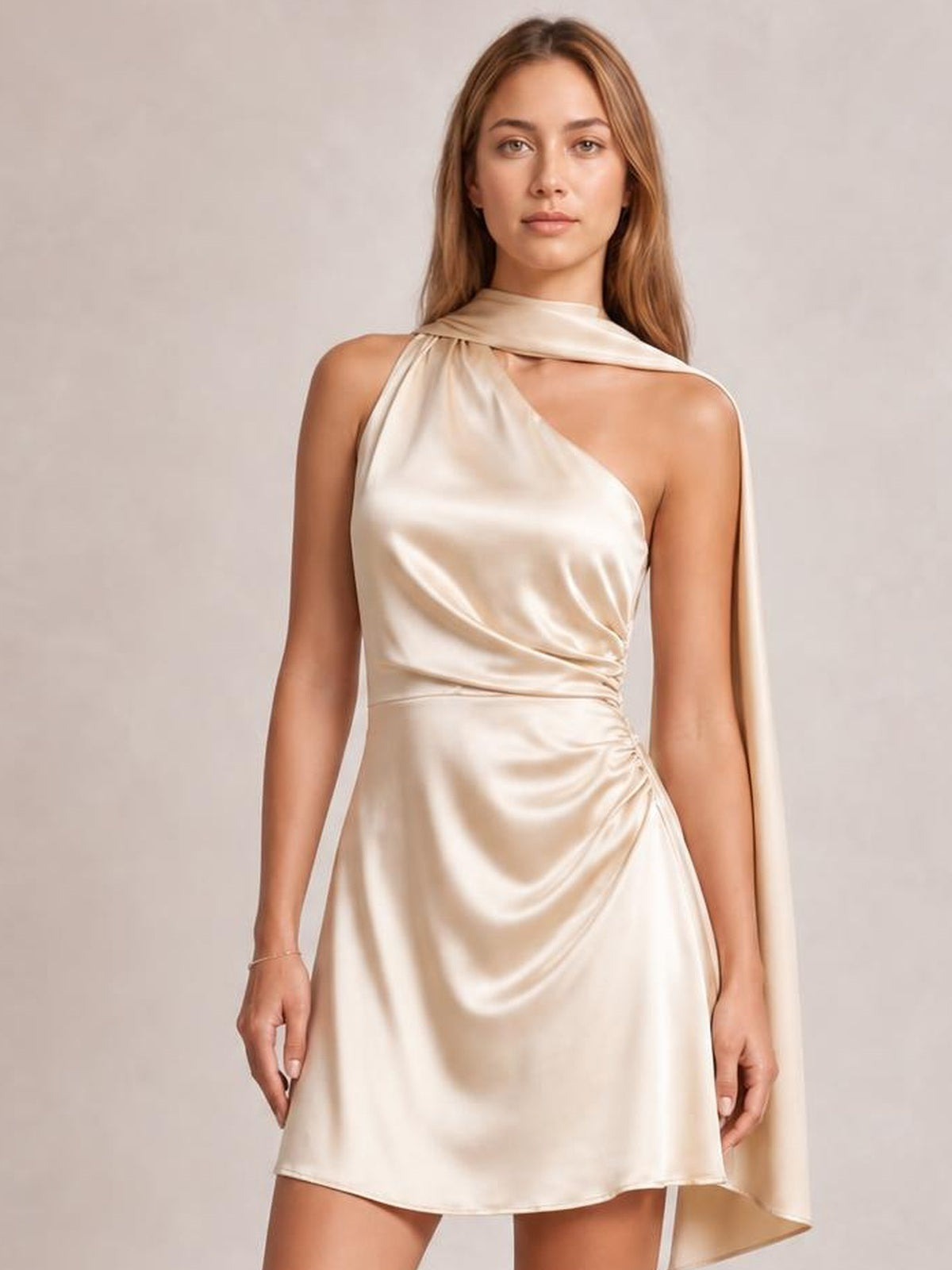 Model stands facing forward in a champagne satin one-shoulder mini dress with a draped neckline, ruched waist, fitted silhouette, and asymmetric hem.