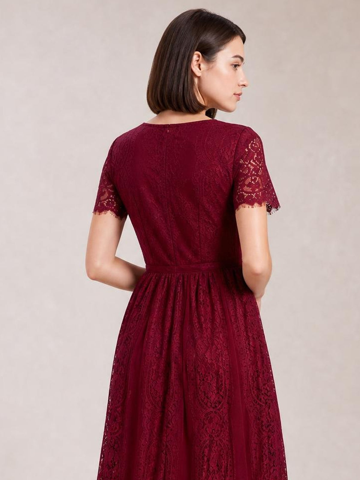A model poses in a burgundy lace maxi dress with scalloped short sleeves, a fitted waist, back zipper, and flowing full skirt.